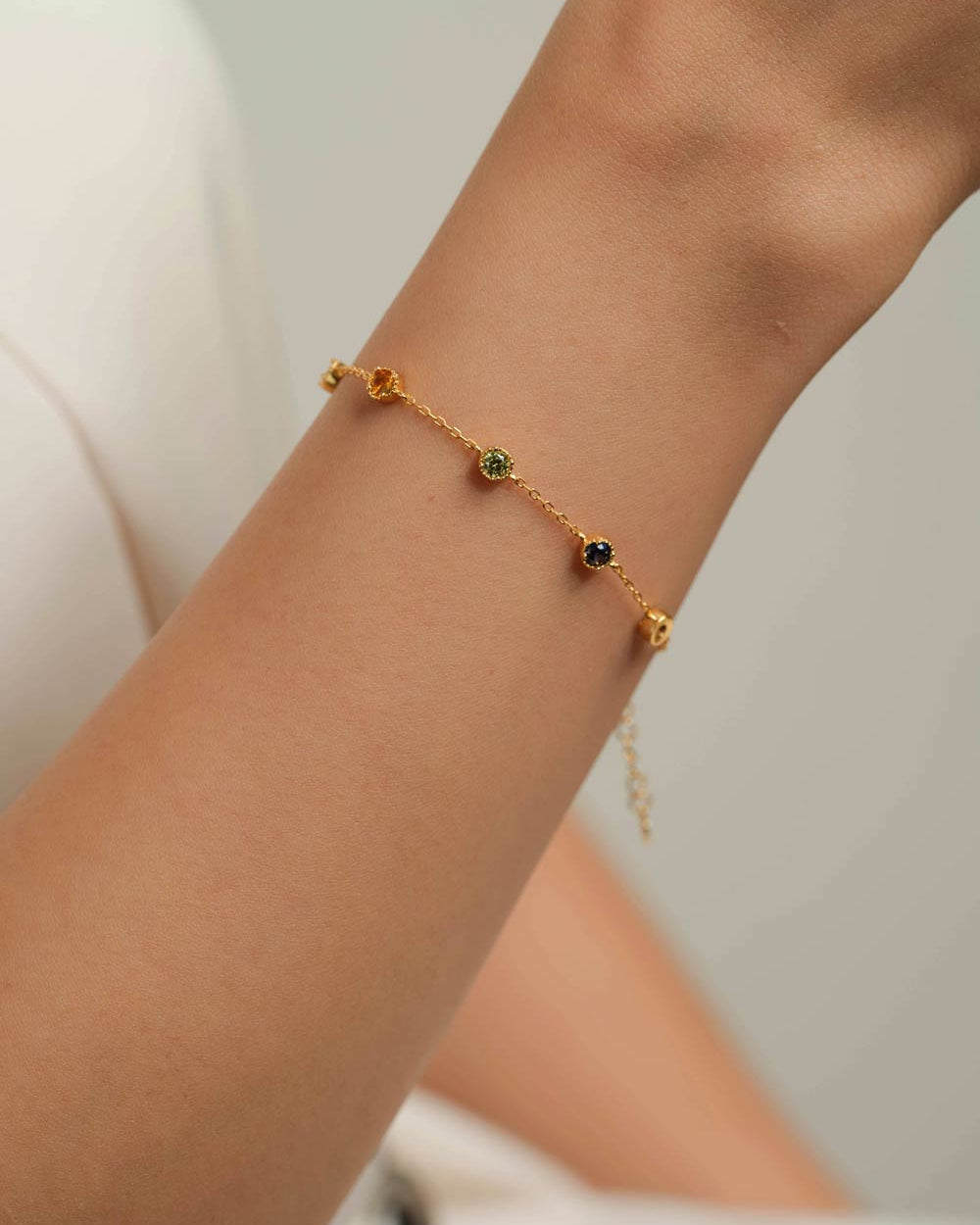 A delicate gold chain bracelet with small colorful gemstone beads, shown worn on a person's wrist.