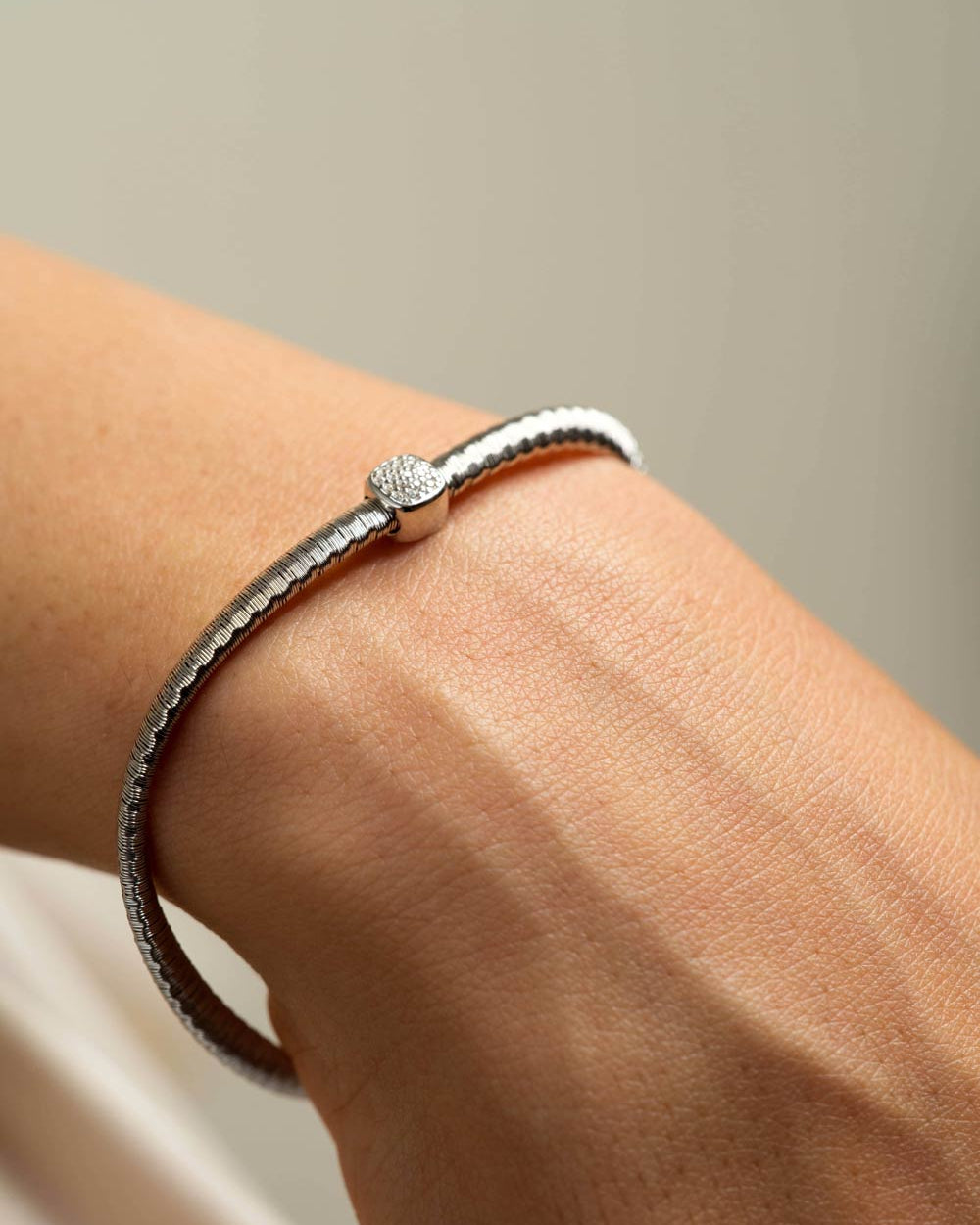 A close-up of a silver snake-bone cuff bracelet worn on a person's wrist, featuring a textured band and a central bead with a small clear stone cluster.