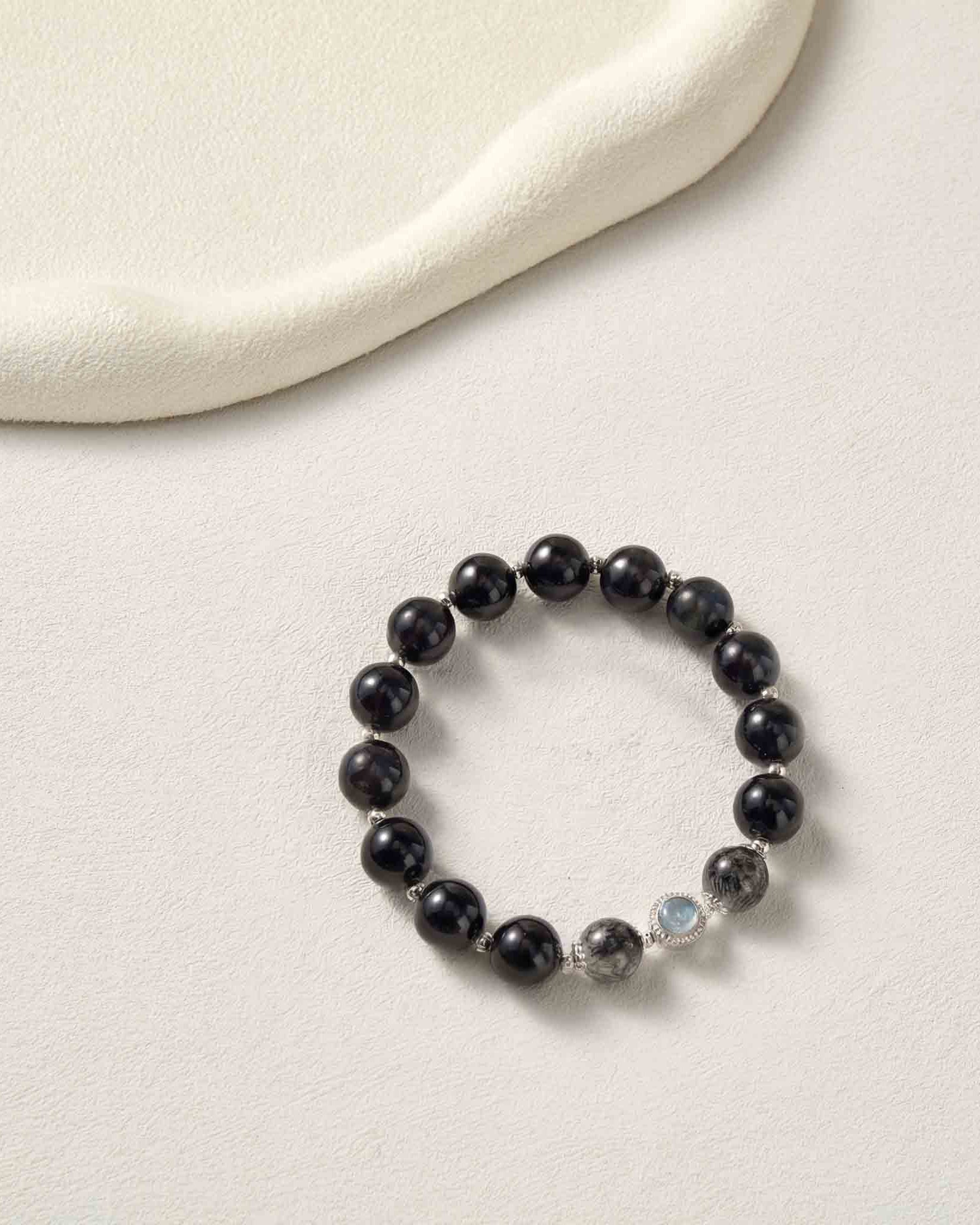 Black beaded bracelet with a small clear bead on a light beige background