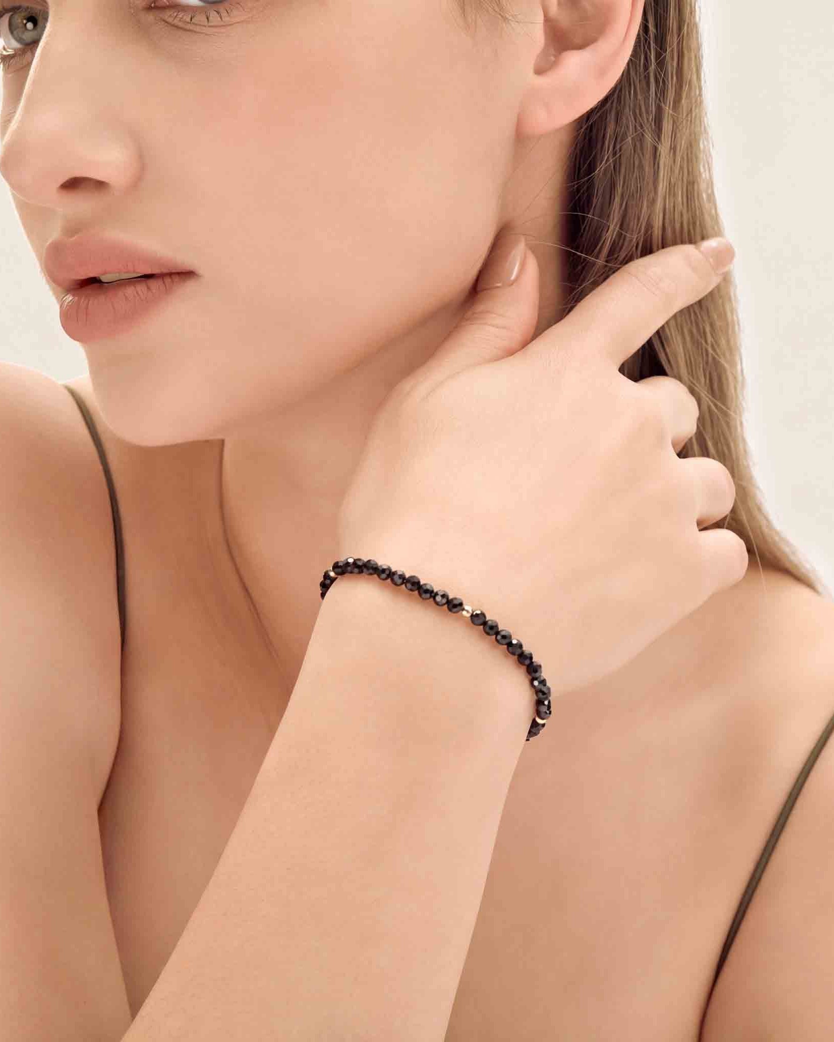 Woman wearing a black beaded bracelet on a neutral background