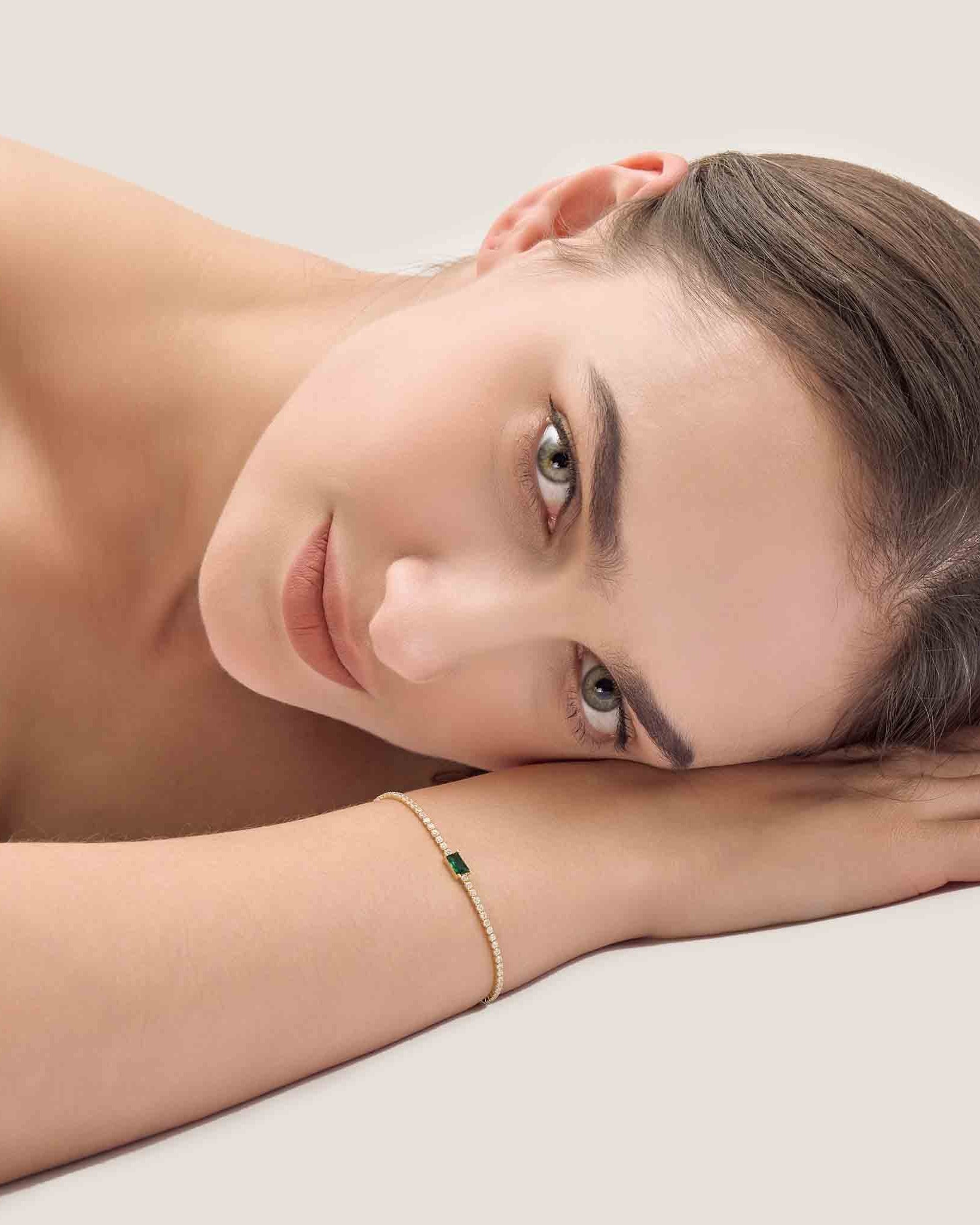 Woman wearing a gold bracelet with a green gemstone on a light background