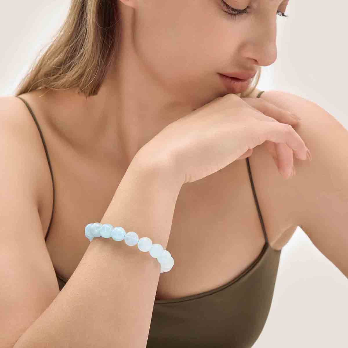 Choodo minimalist natural 11mm Aquamarine crystal beaded bracelet showing unique blue on a model's wrist, styled with a luxurious emerald green silk dress.