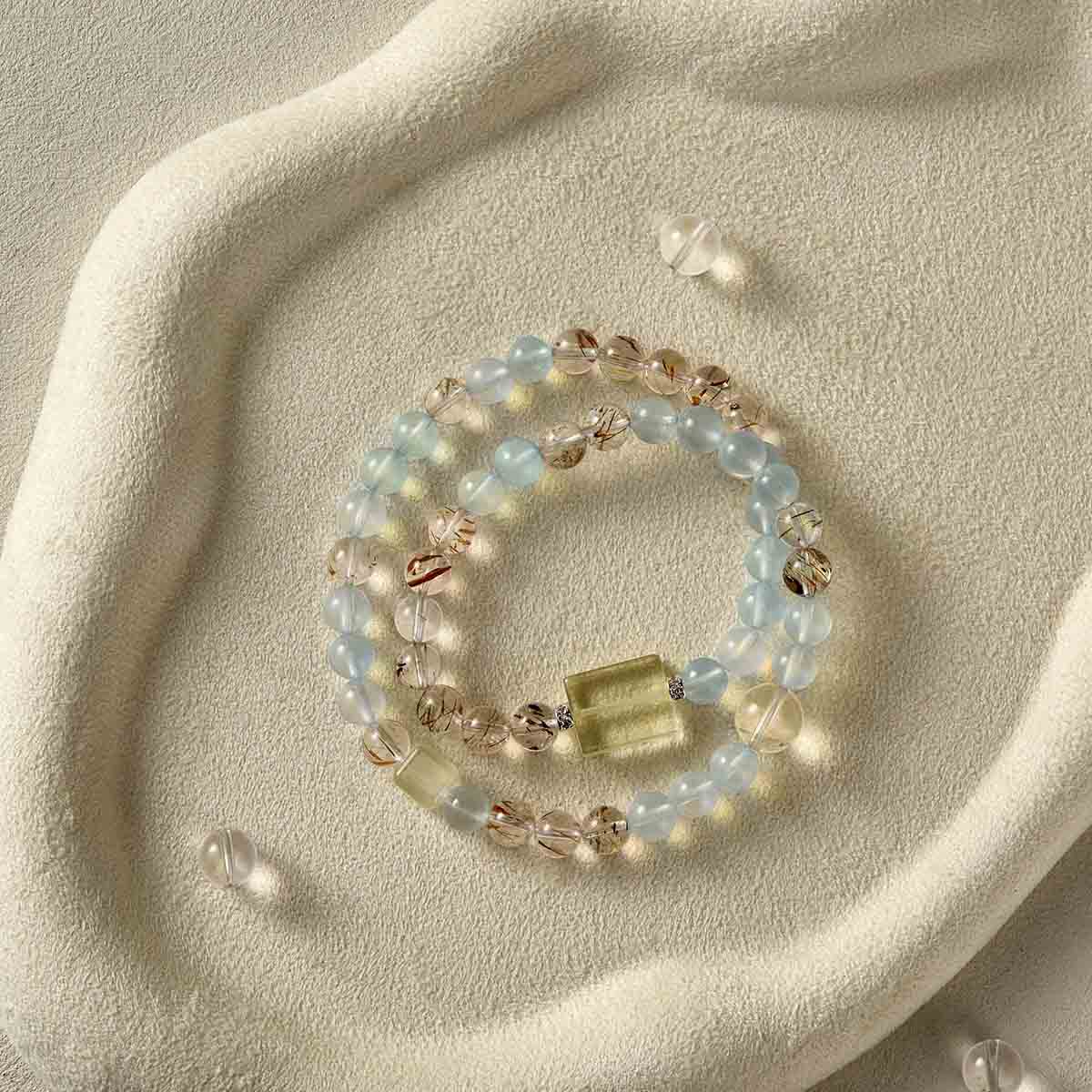 Still life photography of Choodo natural Aquamarine and Clear Quartz crystal double wrap bracelet laid flat on an oatmeal velvet jewelry display tray, premium organic texture contrast