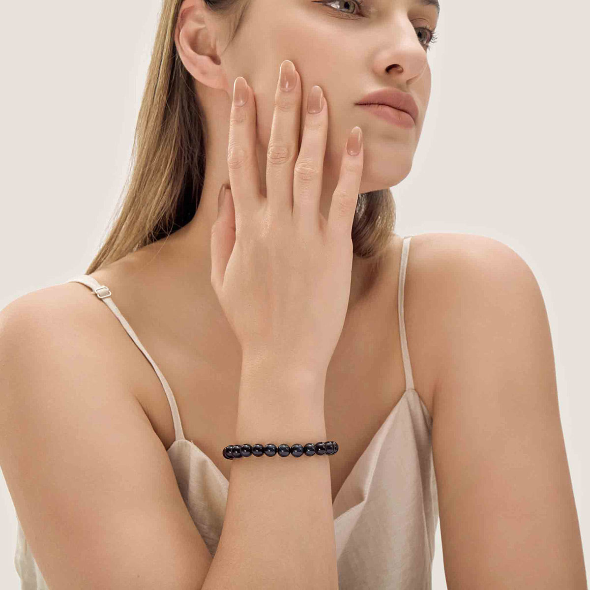Choodo minimalist natural Gold Sheen Obsidian crystal bracelet styled on a model's wrist, paired with a luxurious emerald white silk dress, premium organic aesthetic.