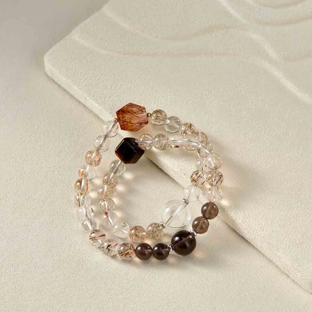 Still life photography of Choodo natural Golden Rutilated Quartz crystal mixed bracelet laid flat on an oatmeal velvet jewelry display pad, capturing the warm golden rutiles and premium textures.