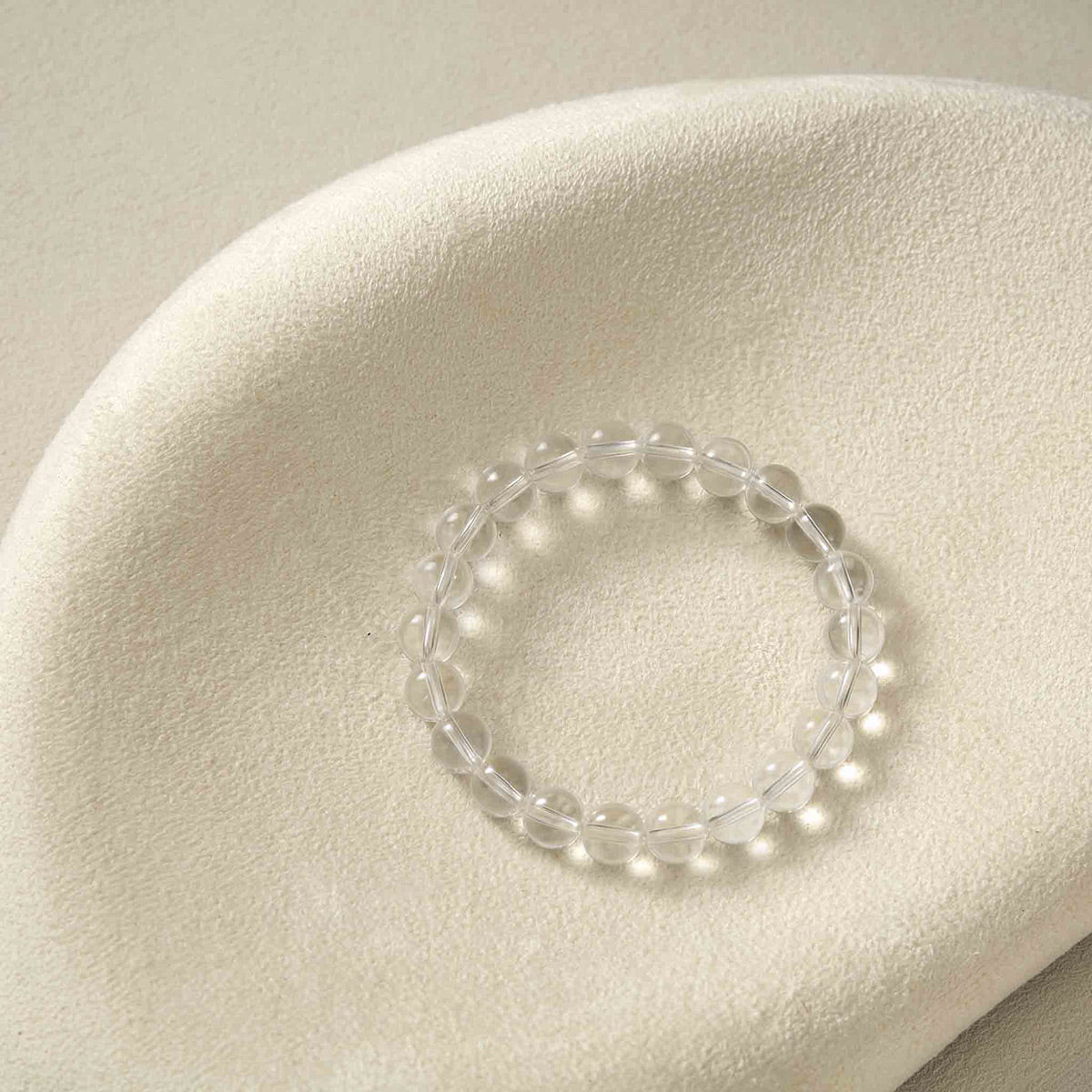 Still life photography of Choodo pure natural Light Clear Quartz crystal beaded bracelet laid flat on an oatmeal velvet jewelry display board, capturing the minimalist premium textures.