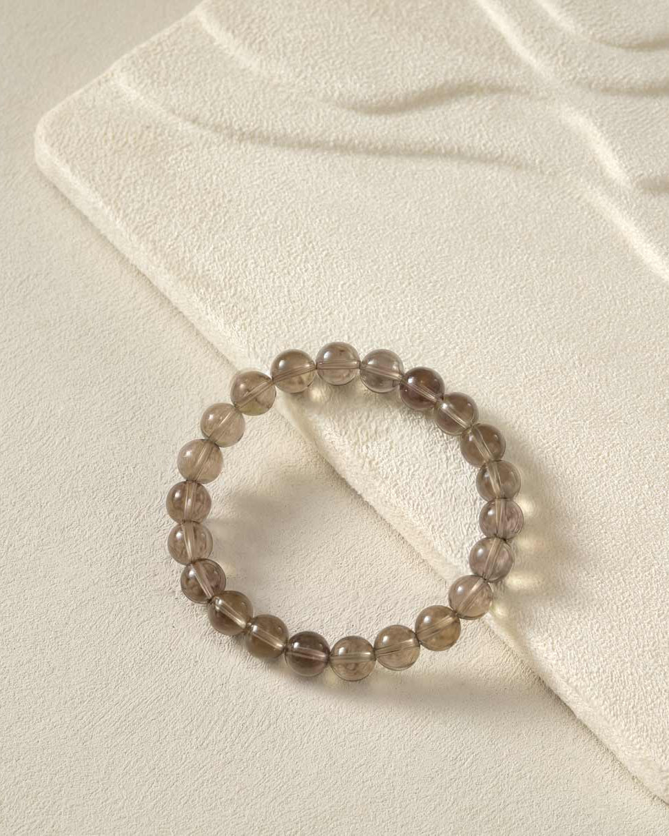 Flat lay of Choodo natural smoky quartz beaded bracelet on a premium oatmeal velvet display board, minimalist aesthetic jewelry.