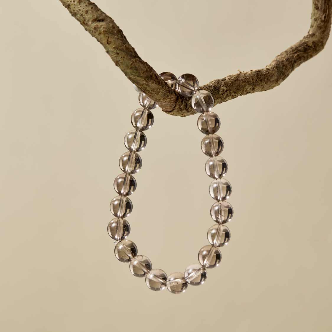 Choodo natural smoky quartz beaded bracelet hanging on a rustic tree branch, organic minimalist jewelry display.