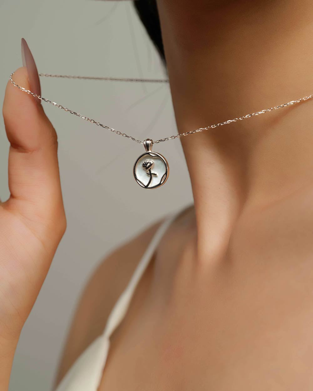 A close-up lifestyle shot of a model wearing a delicate silver chain necklace with a circular pendant featuring a black silhouette of a woman's profile.
