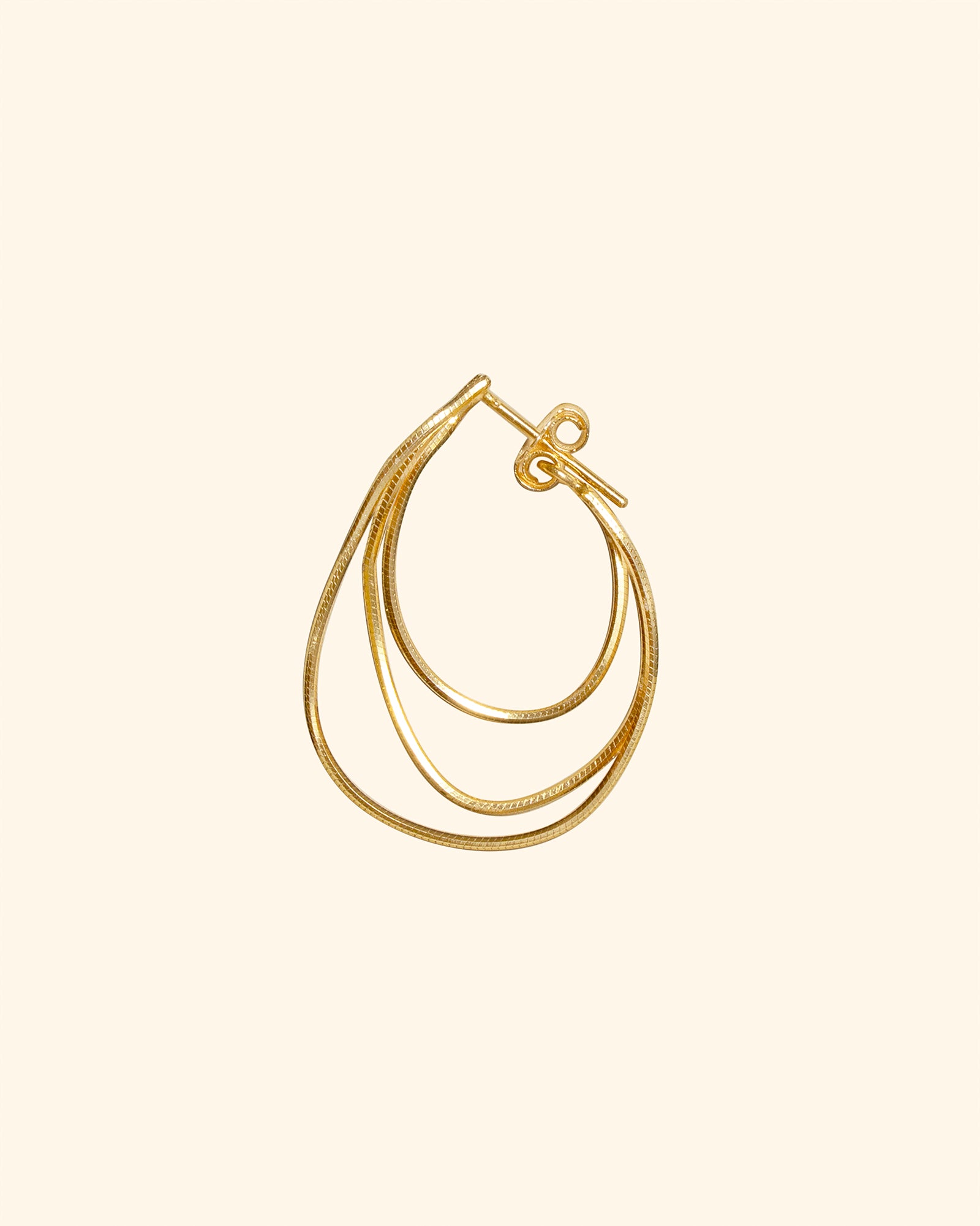 A single gold-toned hoop earring with a small front clasp, photographed on a plain warm off-white background.