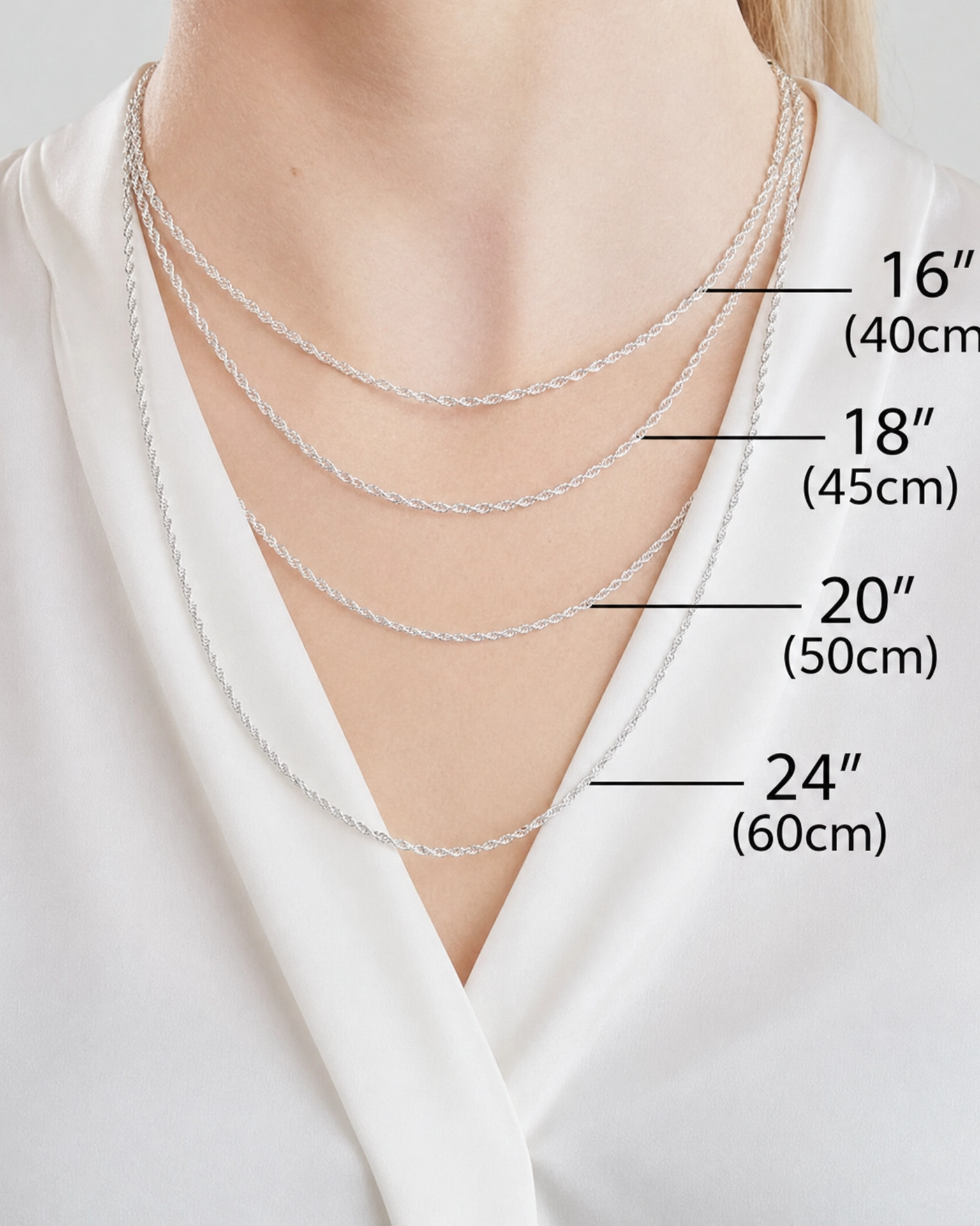 A close-up of a person's neck and upper chest wearing three layered silver chains at different lengths, with text labels indicating 16 inches (40 cm), 18 inches (45 cm), 20 inches (50 cm), and 24 inches (60 cm).