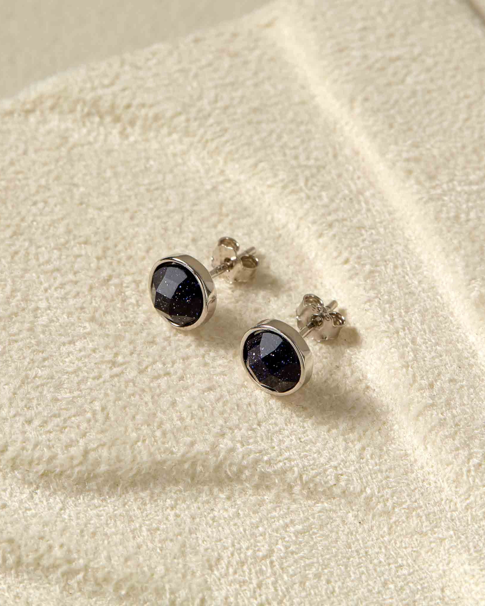 Pair of silver earrings with black gemstones on a textured beige surface