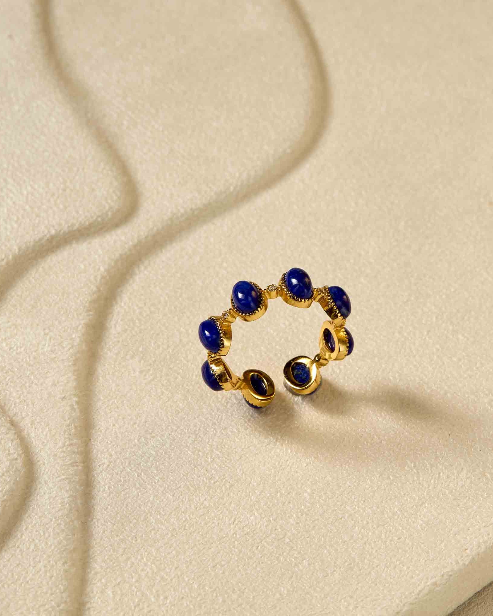 Gold ring with blue stones on a textured beige surface