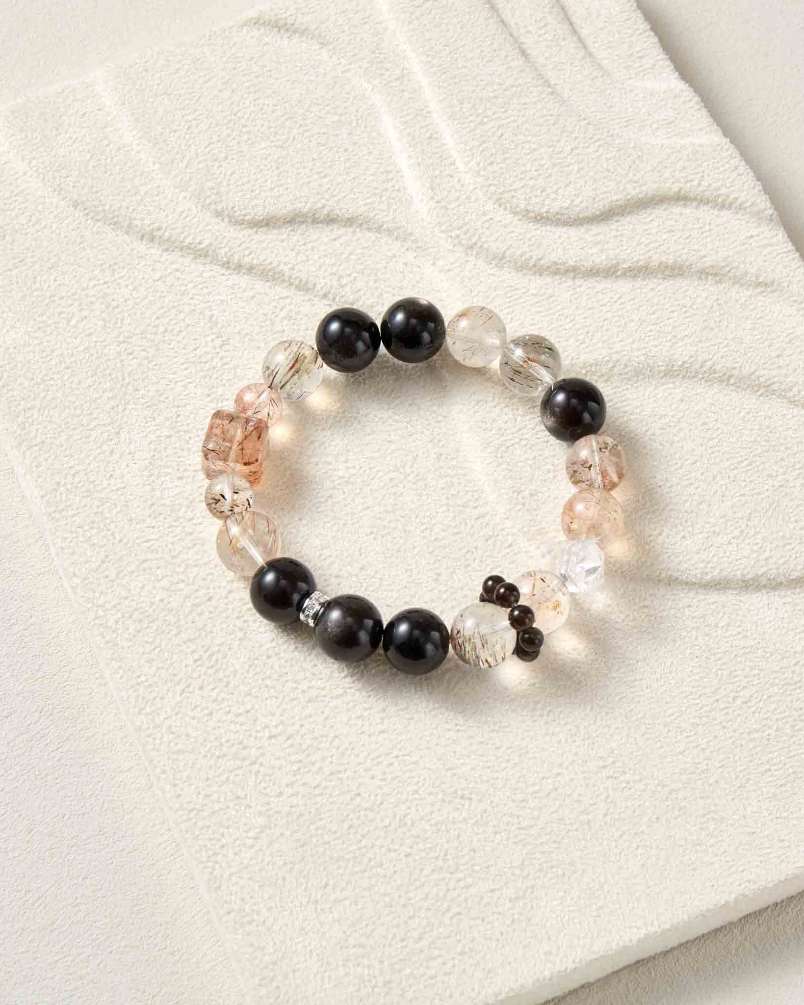 Beaded bracelet with black, clear, and pink beads on a white fabric background