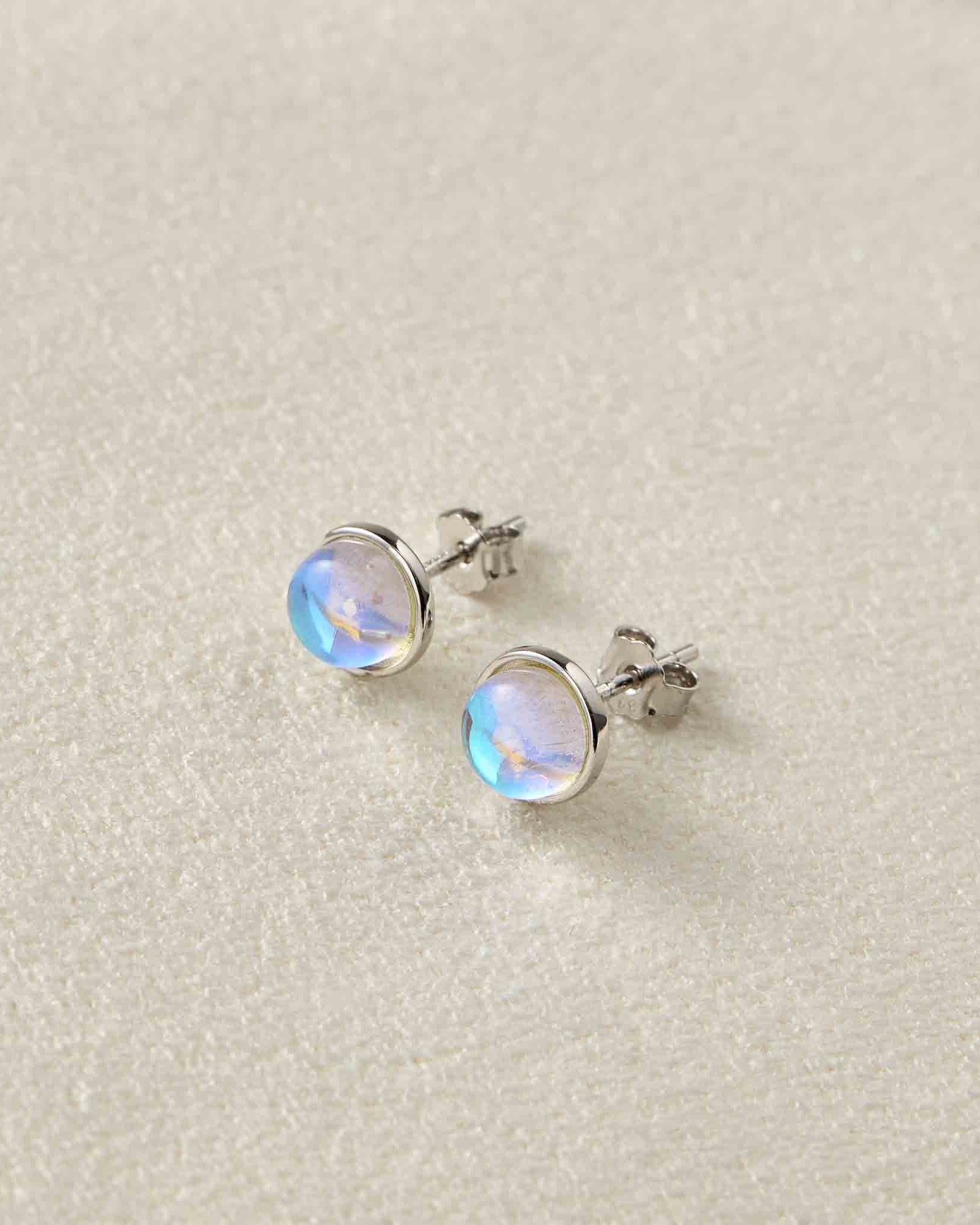 Pair of silver earrings with rainbow moonstone stones on a light gray background