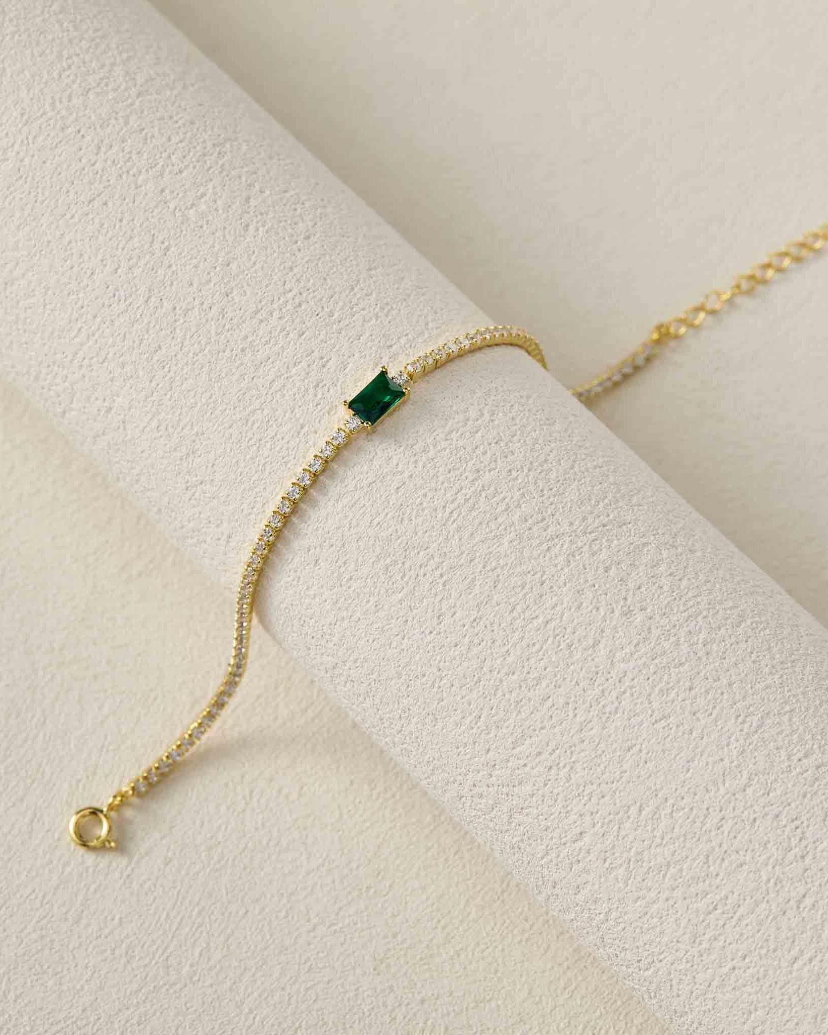 Gold bracelet with a green gemstone on a light beige surface