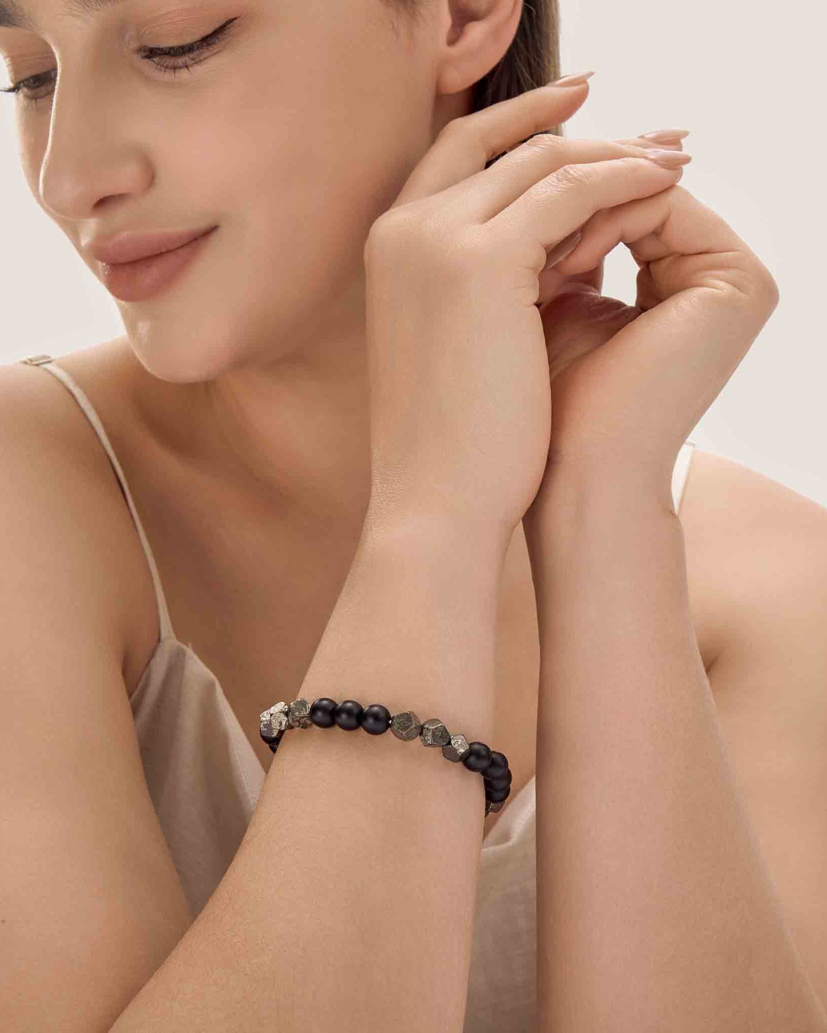 Woman wearing a black beaded bracelet on her wrist with a neutral background