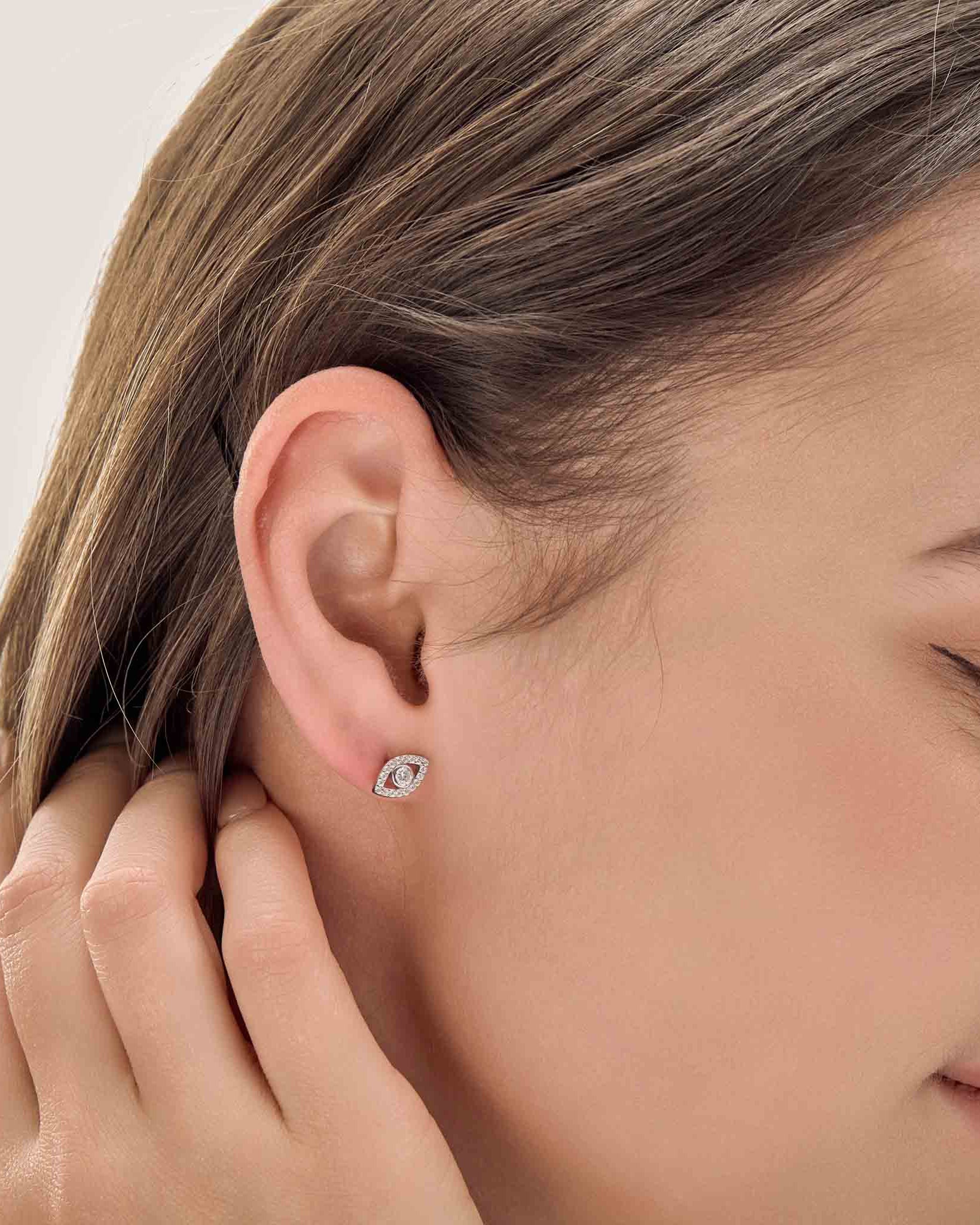Close-up of a person wearing a diamond stud earring on a plain background