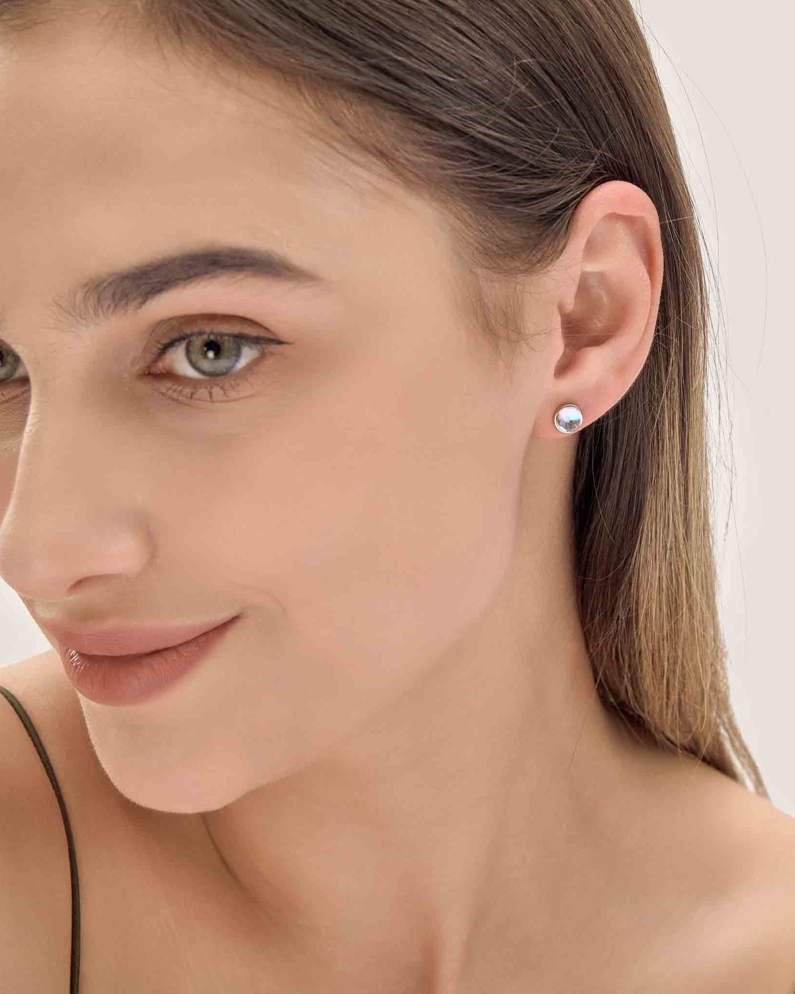 Close-up of a woman wearing a small round earring on a plain background