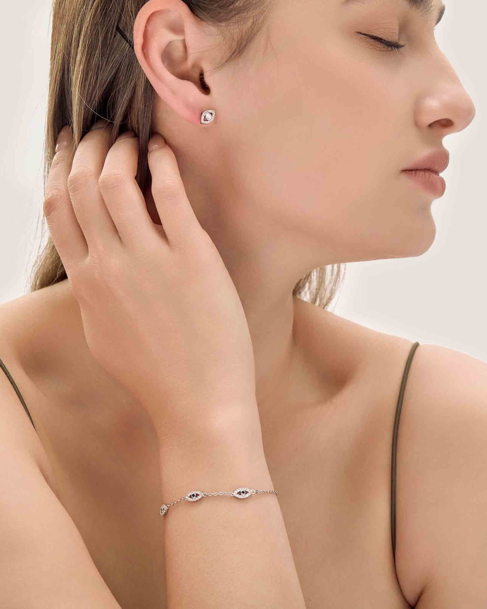 Woman wearing a silver earring and bracelet on a plain background
