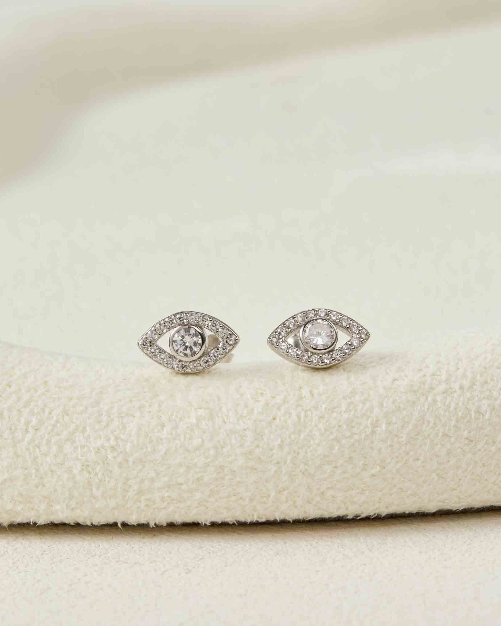 Silver eye-shaped earrings on a white fabric background
