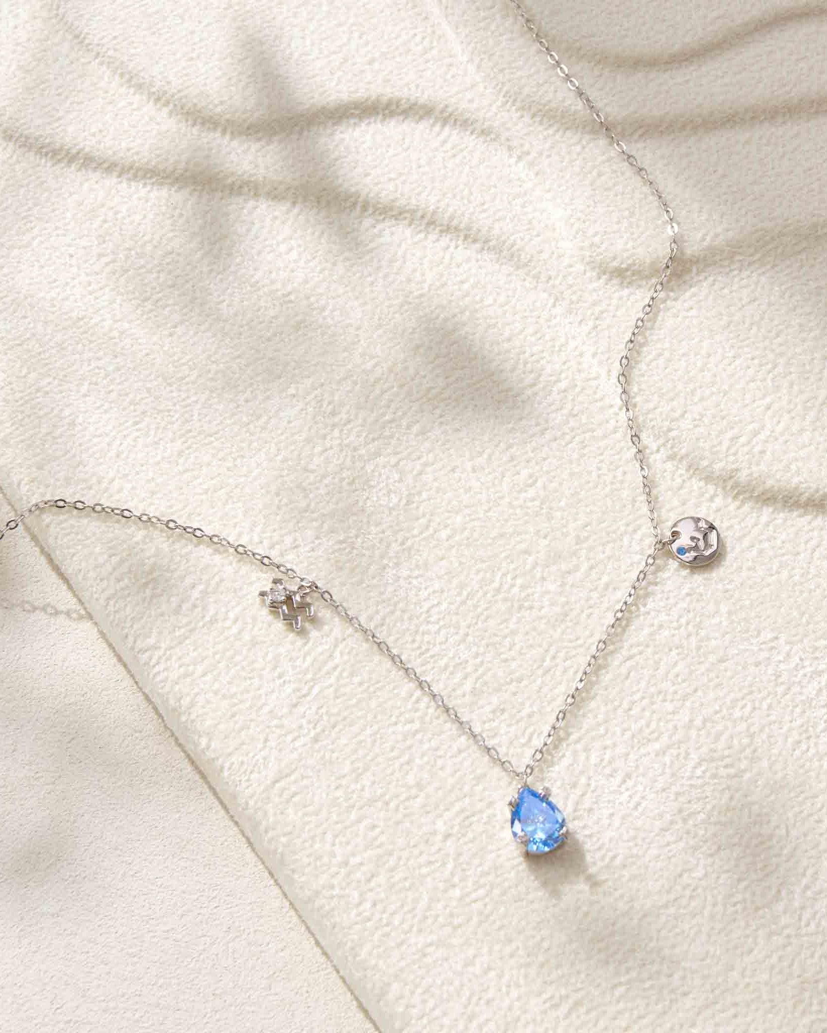 Necklace with a blue teardrop pendant on a white fabric background
