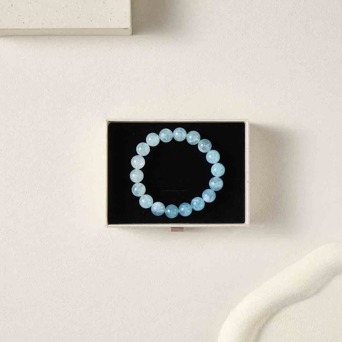 Still life photography of Choodo 11mm natural Aquamarine gemstone beaded bracelet displayed in a premium black foam jewelry gift box, highlighting the stunning natural gradient color in each bead.