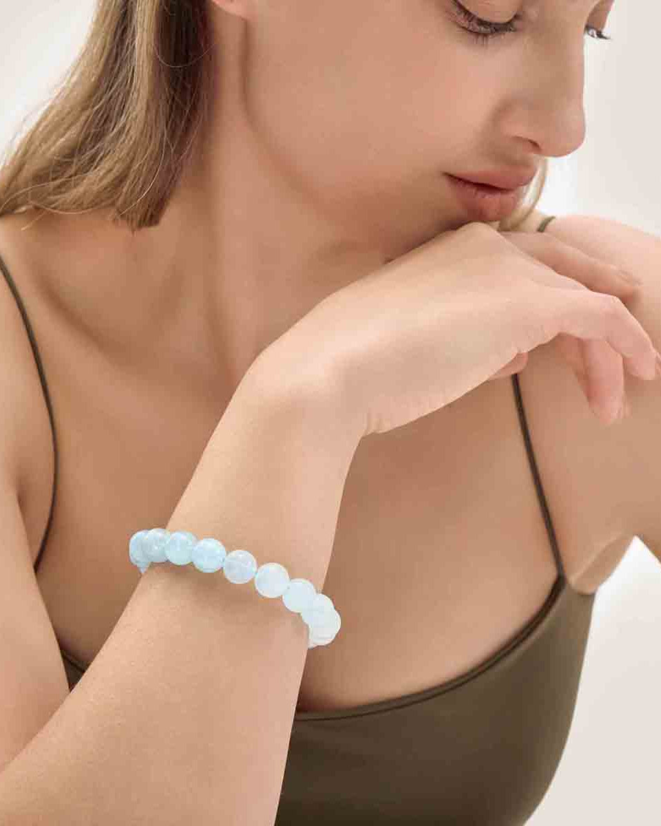Choodo minimalist natural 11mm Aquamarine crystal beaded bracelet showing unique blue on a model's wrist, styled with a luxurious emerald green silk dress.