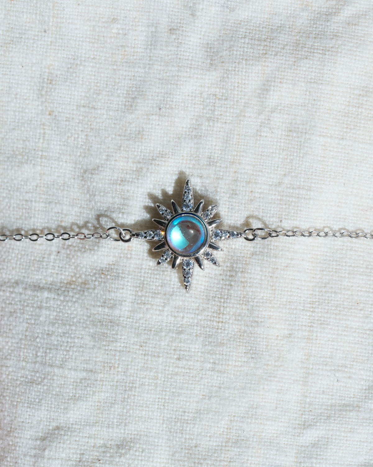 Close-up detail of Choodo 925 sterling silver sun pendant necklace with natural moonstone on cream background