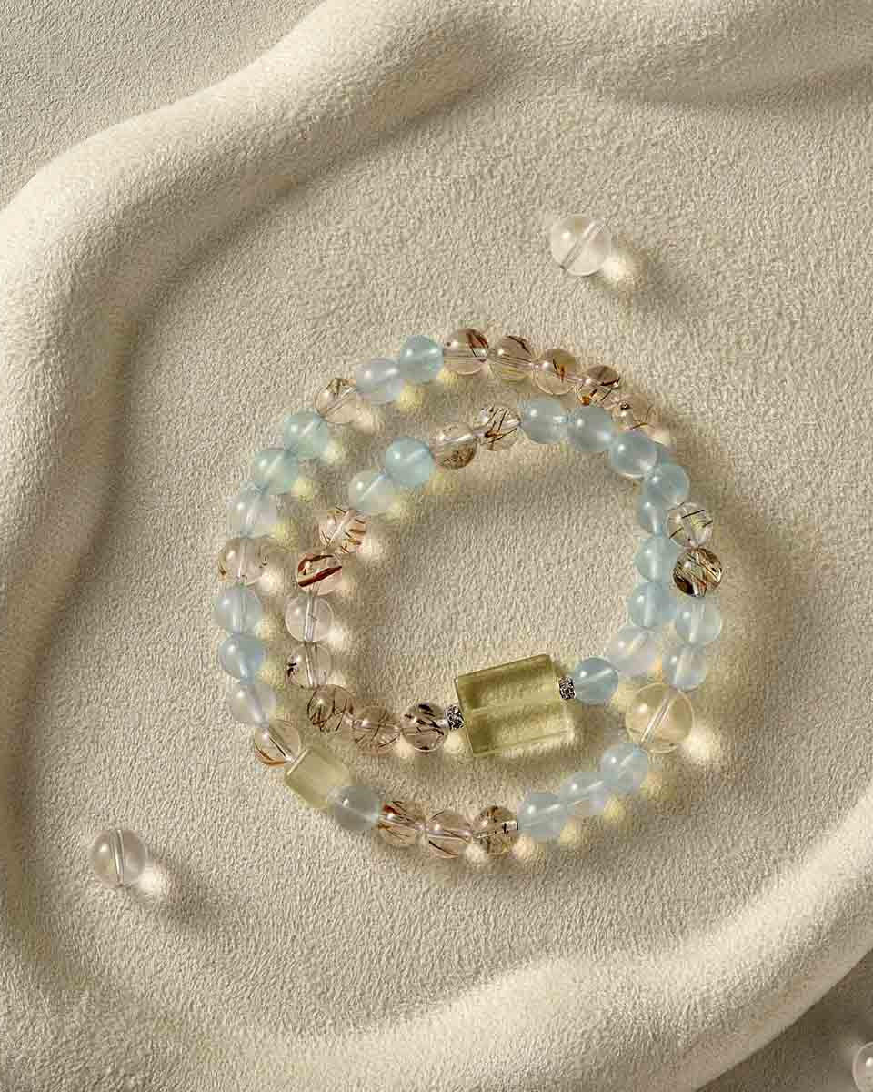 Still life photography of Choodo natural Aquamarine and Clear Quartz crystal double wrap bracelet laid flat on an oatmeal velvet jewelry display tray, premium organic texture contrast