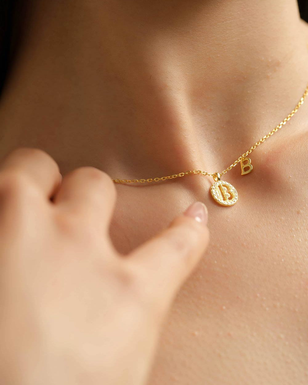 Close-up of a model wearing Choodo gold plated sterling silver dual 'B' letter pendant necklace on the collarbone, personalized jewelry