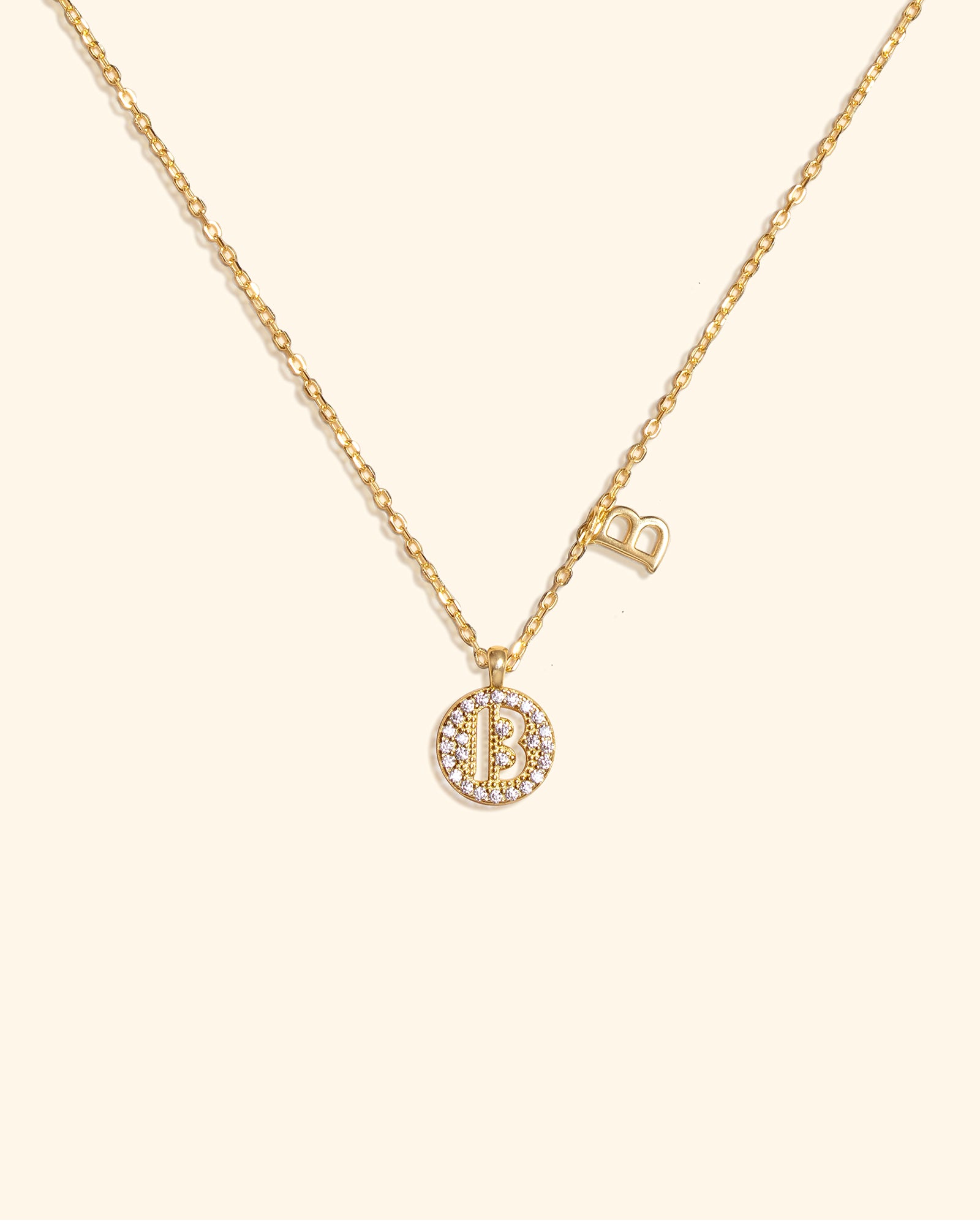 Choodo gold plated sterling silver necklace with two pendants: a CZ stone-paved 'B' disc and a smaller 'B' charm on a cream background