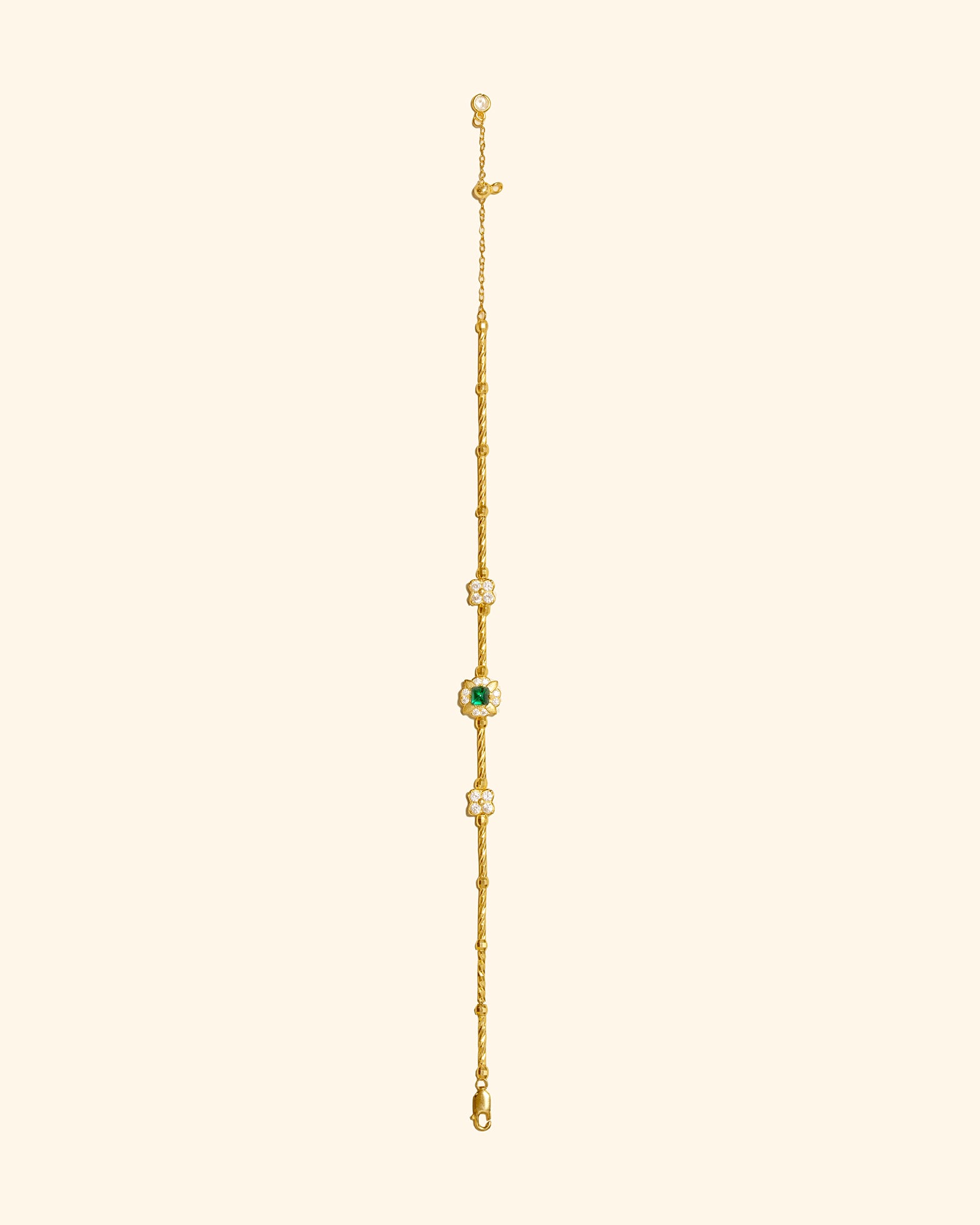 A delicate gold chain bracelet featuring a central round green gemstone surrounded by small zircons, set against a solid pale cream background.