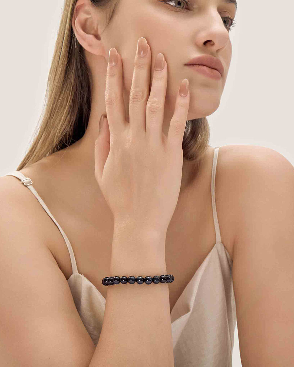 Choodo minimalist natural Gold Sheen Obsidian crystal bracelet styled on a model's wrist, paired with a luxurious emerald white silk dress, premium organic aesthetic.