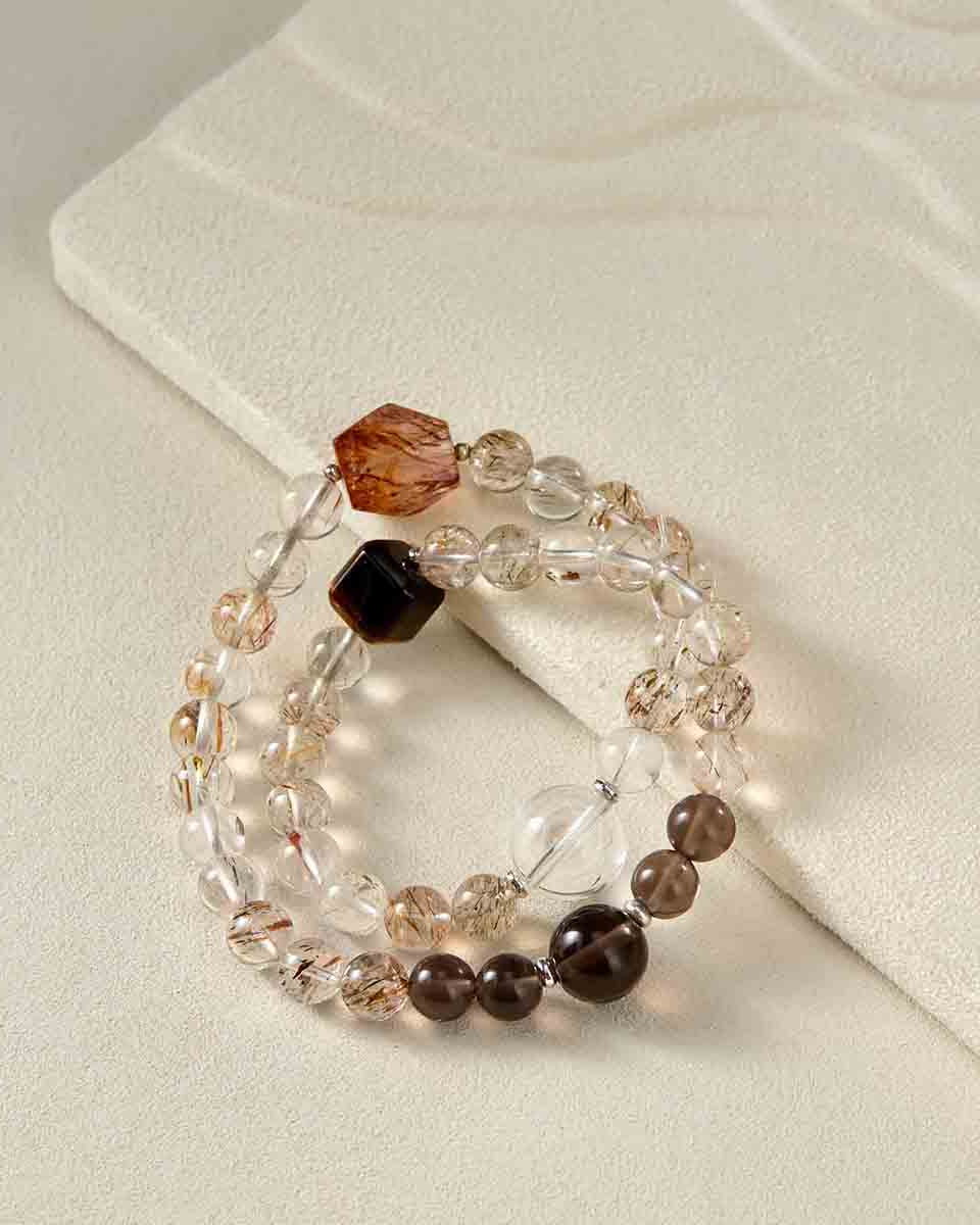 Still life photography of Choodo natural Golden Rutilated Quartz crystal mixed bracelet laid flat on an oatmeal velvet jewelry display pad, capturing the warm golden rutiles and premium textures.