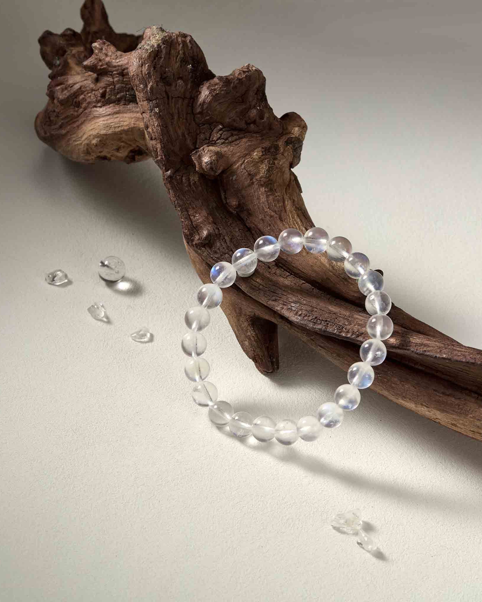 Still life photography of Choodo pure natural Madagascar Rainbow Moonstone crystal beaded bracelet laid flat on a rustic dry tree branch, capturing the iridescent colorful glow.