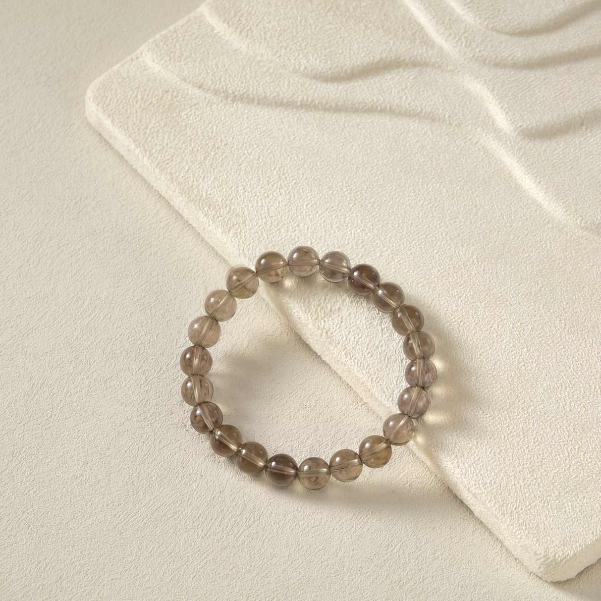 Flat lay of Choodo natural smoky quartz beaded bracelet on a premium oatmeal velvet display board, minimalist aesthetic jewelry.