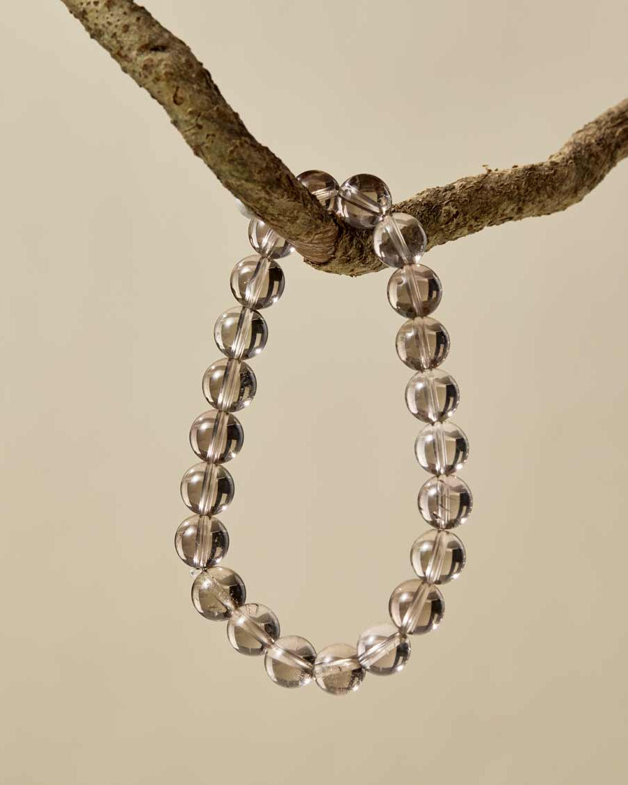Choodo natural smoky quartz beaded bracelet hanging on a rustic tree branch, organic minimalist jewelry display.