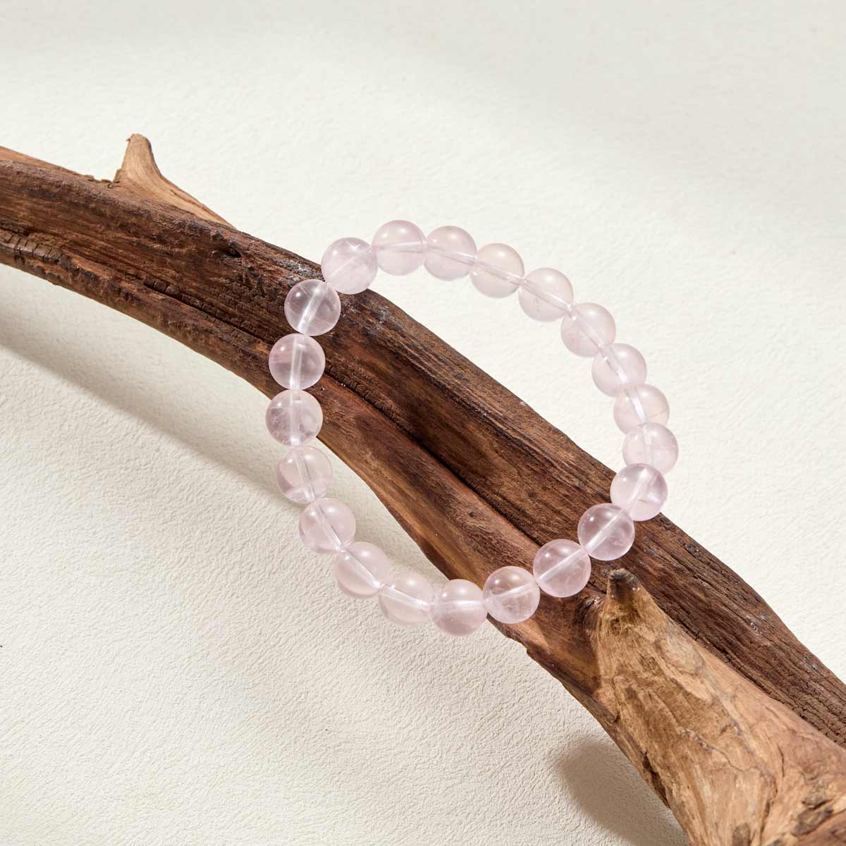 Still life photography of Choodo Strawberry Quartz crystal bracelet laid flat on a rustic natural tree branch display, organic sweet jewelry aesthetics, nature-inspired design