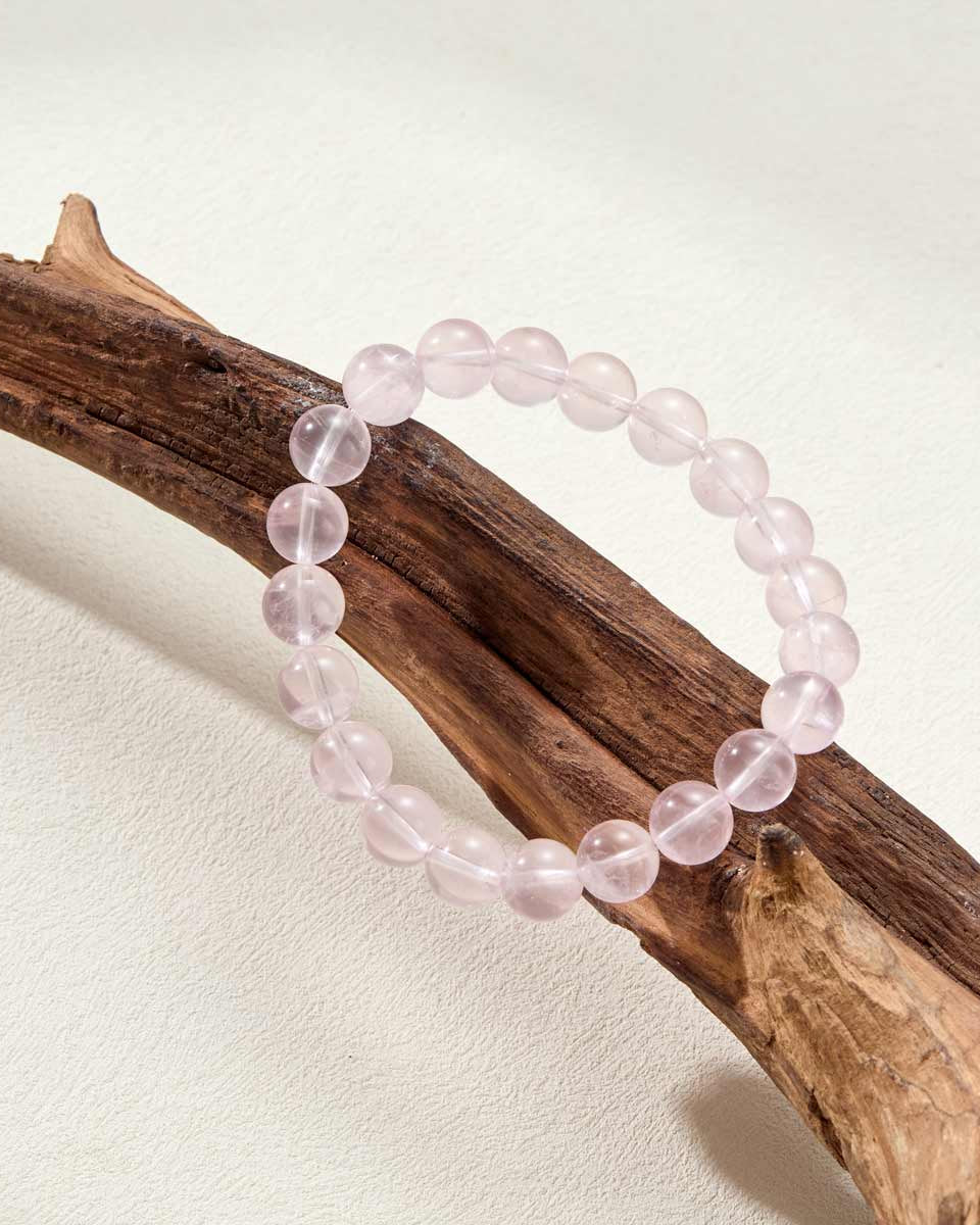 Still life photography of Choodo Strawberry Quartz crystal bracelet laid flat on a rustic natural tree branch display, organic sweet jewelry aesthetics, nature-inspired design