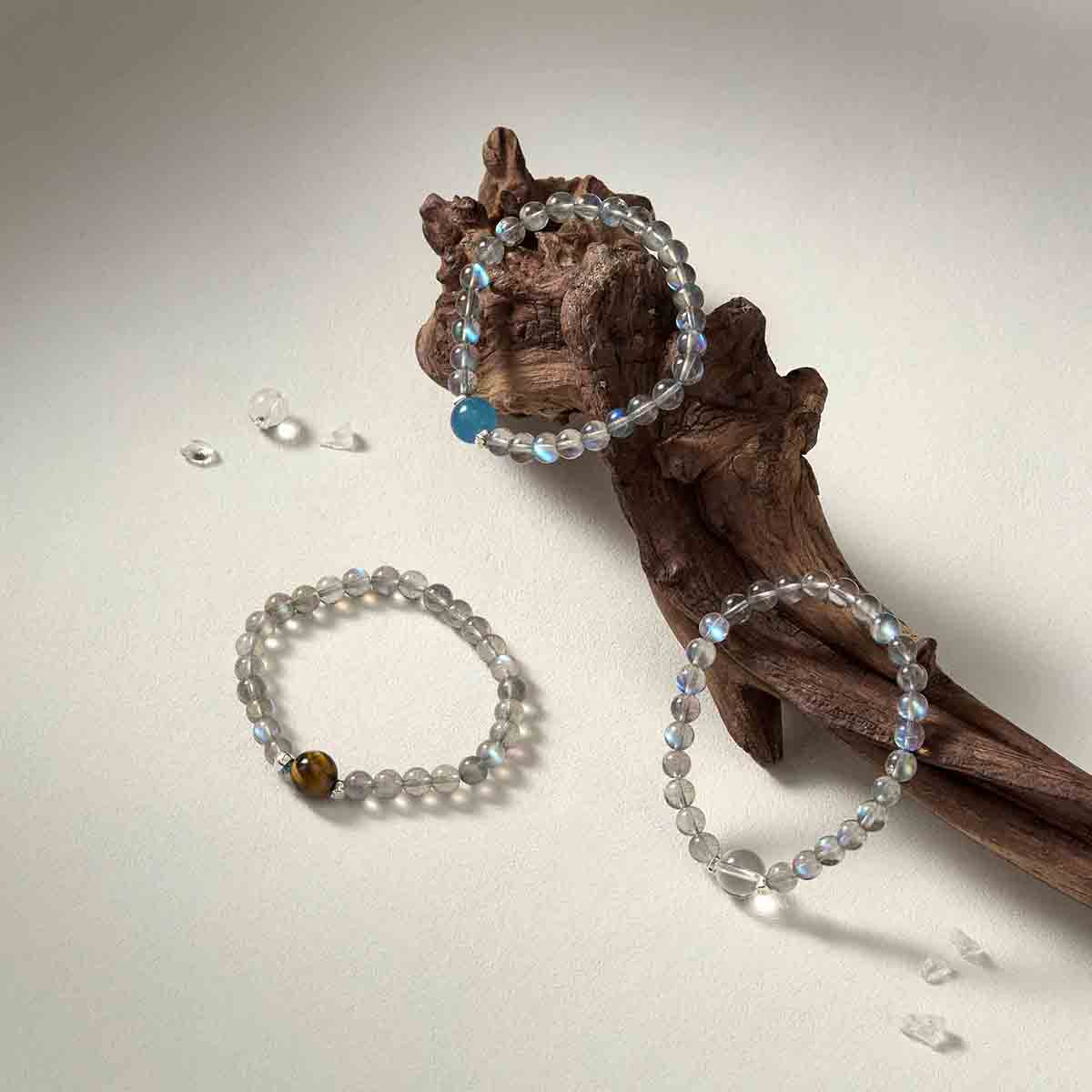 Still life photography of Choodo Orbit Collection featuring 11mm Tiger's Eye, Clear Quartz, and Aquamarine bracelets laid flat on a rustic natural tree branch.