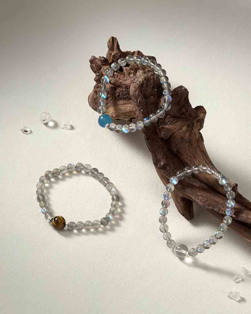 Still life photography of Choodo Orbit Collection featuring 11mm Tiger's Eye, Clear Quartz, and Aquamarine bracelets laid flat on a rustic natural tree branch.