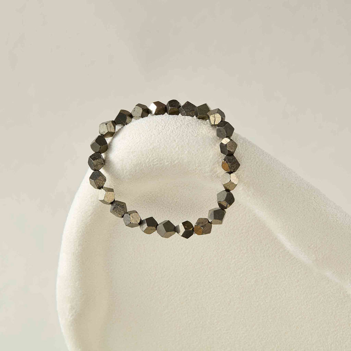 Still life photography of Choodo pure natural Pyrite metallic gemstone beaded bracelet laid flat on an oatmeal velvet display pad, architectural minimalist jewelry art.