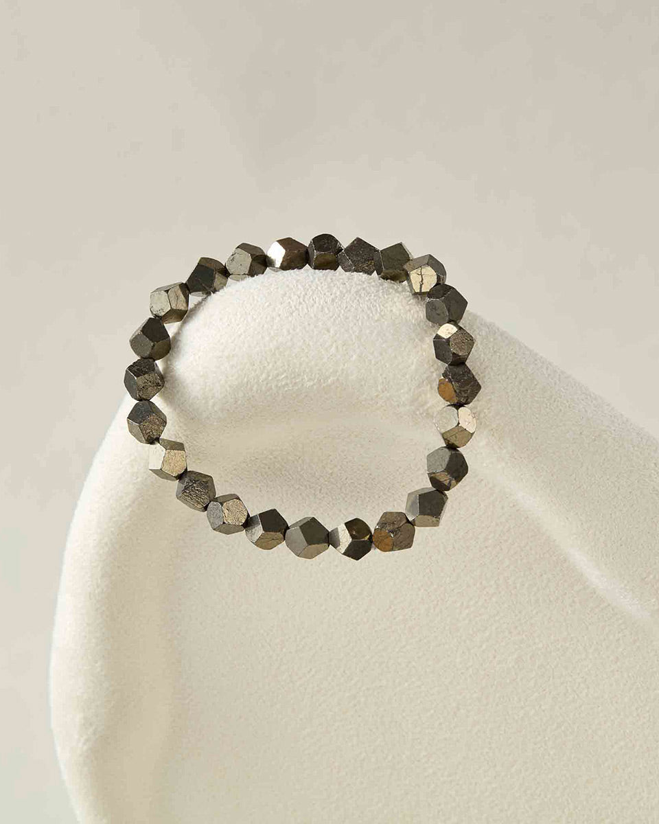 Still life photography of Choodo pure natural Pyrite metallic gemstone beaded bracelet laid flat on an oatmeal velvet display pad, architectural minimalist jewelry art.