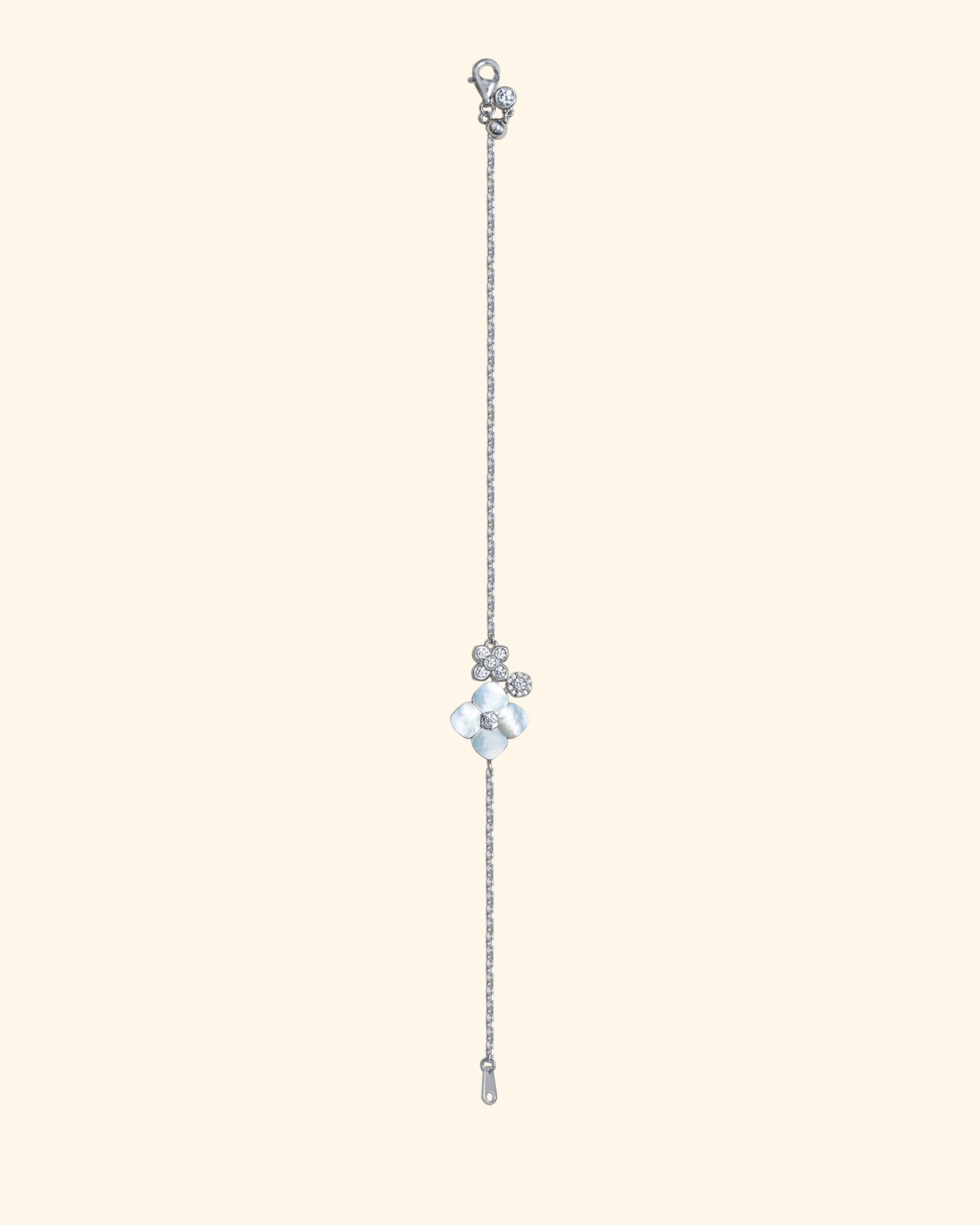 A delicate silver-toned chain earring with a central clear faceted mother of pearl and small flower shaped bead accents, shown against a solid pale cream background.