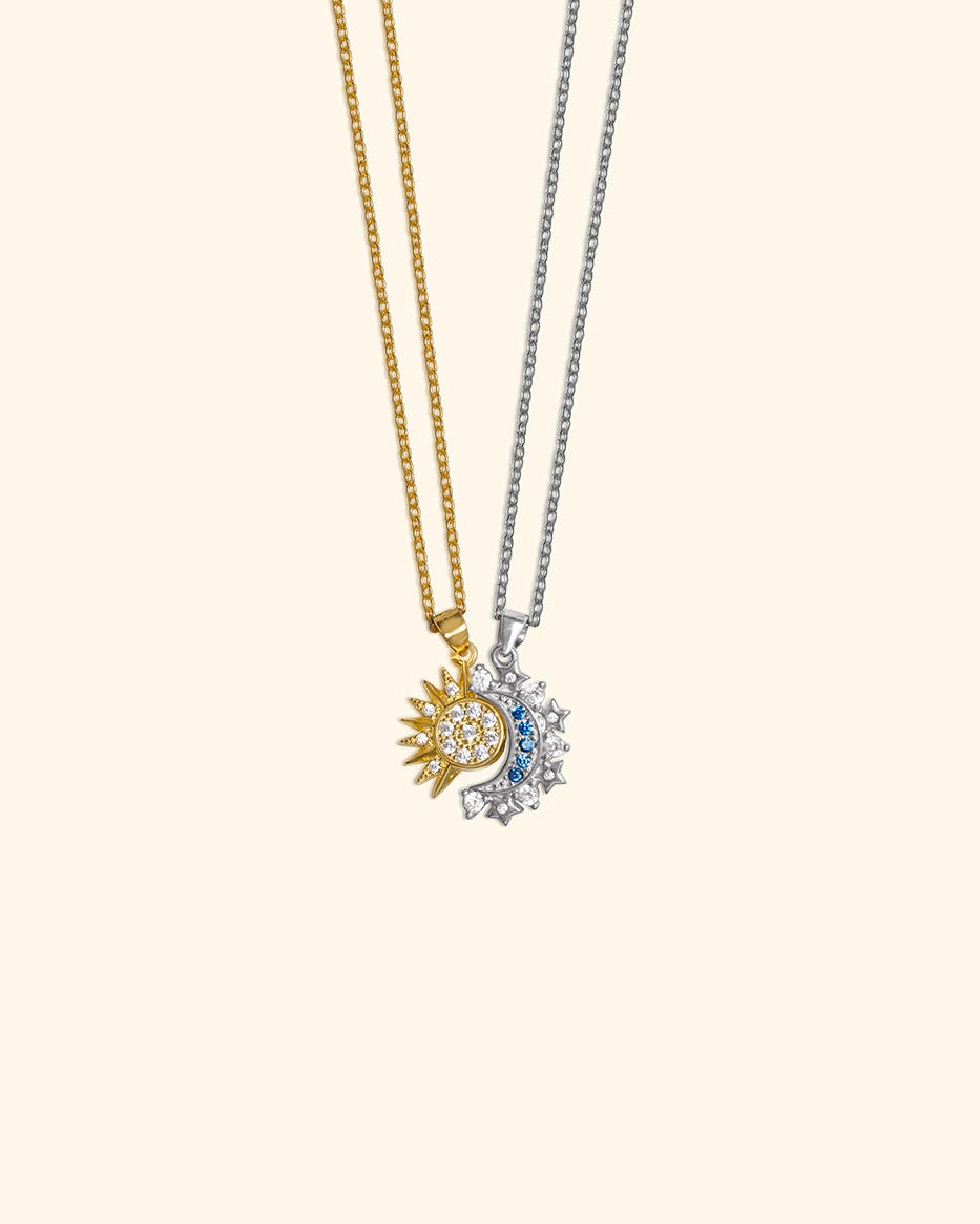 Two delicate pendant necklaces on a plain light beige background. One necklace is gold-toned with a sun and crescent moon pendant, and the other is silver-toned with a crescent moon and small shiny zircons.