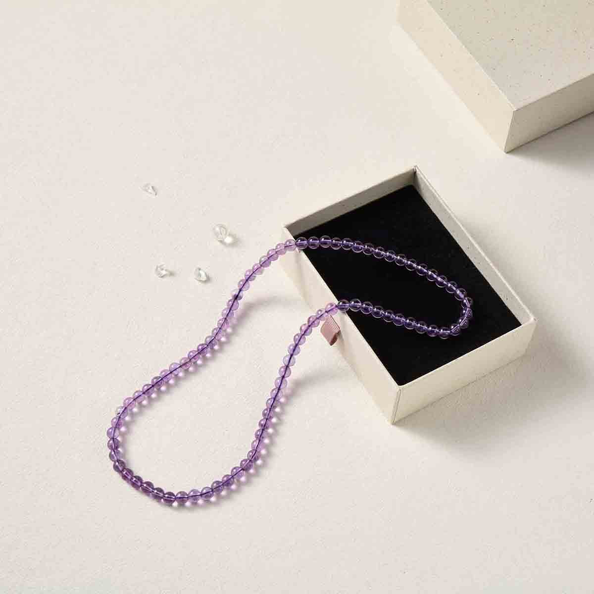 Still life photography of Choodo natural Amethyst crystal three-layer beaded bracelet laid flat to showcase length in a premium black foam jewelry box, high-contrast premium luxury textures.