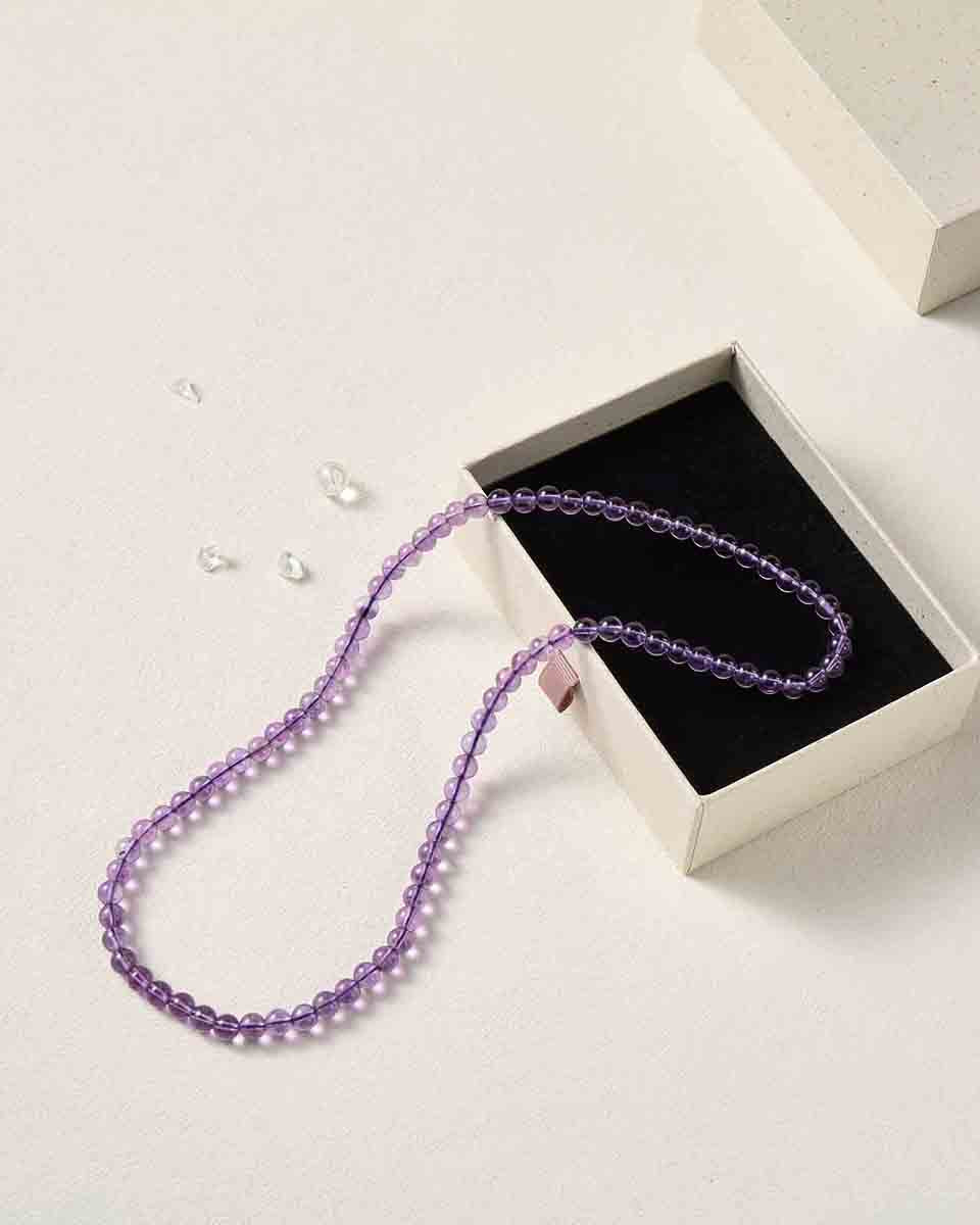 Still life photography of Choodo natural Amethyst crystal three-layer beaded bracelet laid flat to showcase length in a premium black foam jewelry box, high-contrast premium luxury textures.