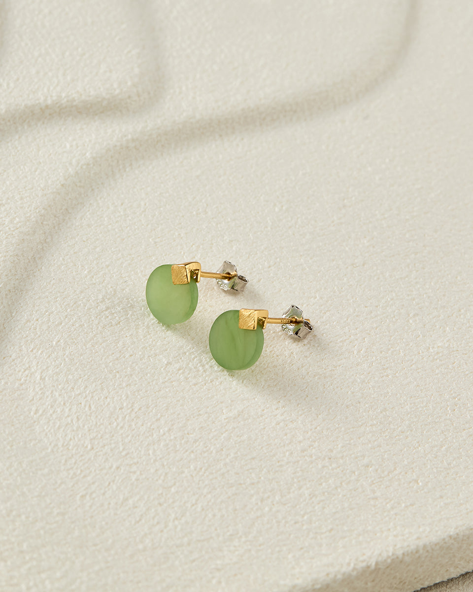 Still life photography of Choodo natural green Jade sterling silver earrings laid flat on a serene beige tabletop, modern intellectual premium vibe.
